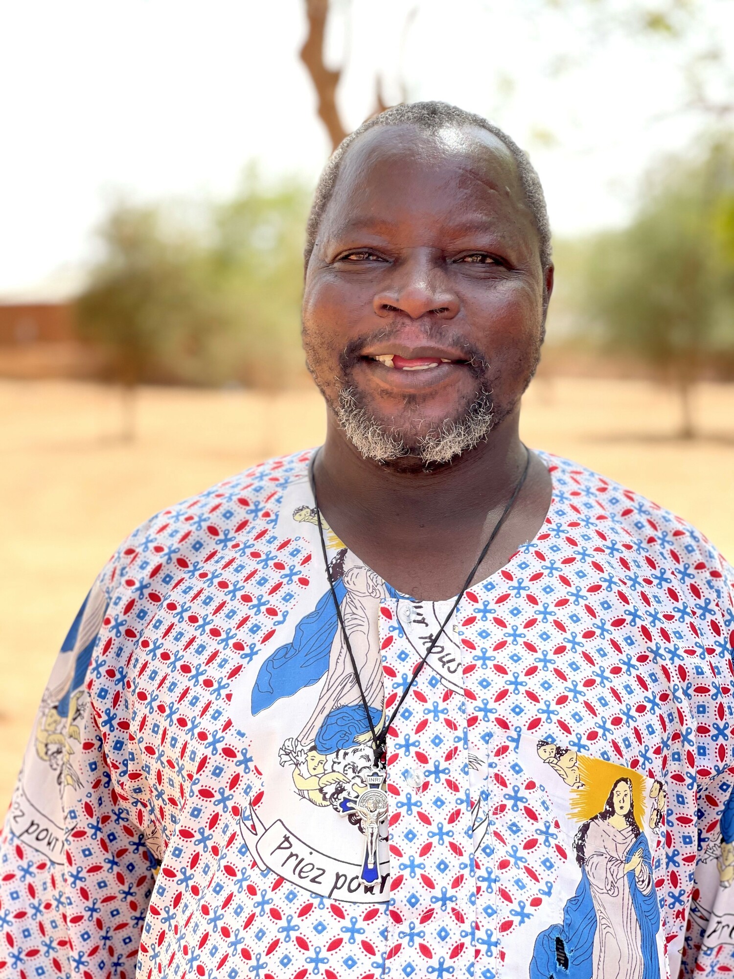 A portrait of a priest in Burkina Faso. He is wearing a white, blue and red shirt
