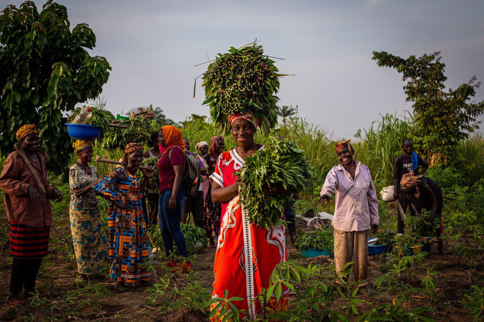 Women stand in field with harvest.