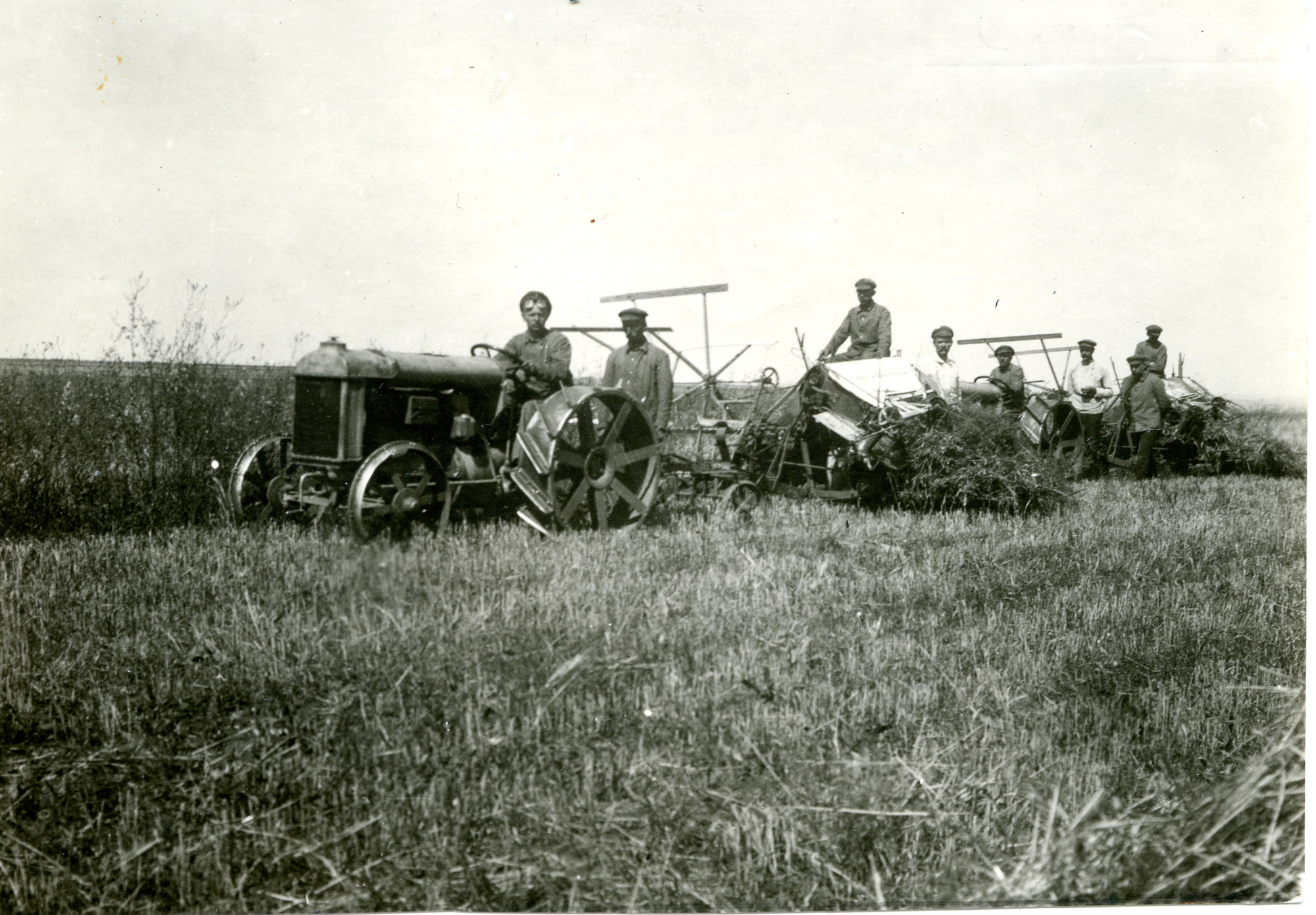 A black and white photo from the 1920s of farmers in a field with tractors