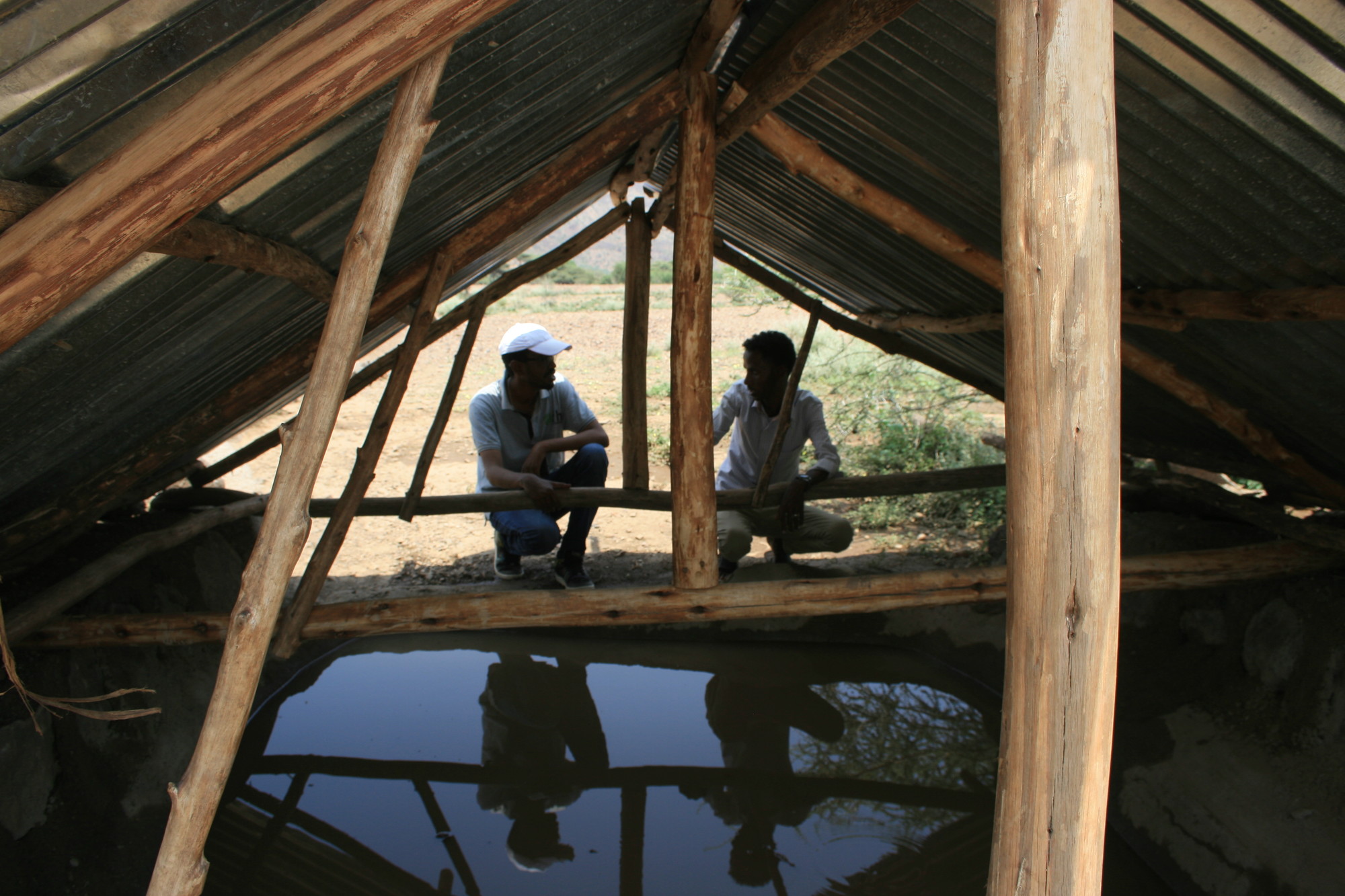 Two people look into a covered, in-ground cistern
