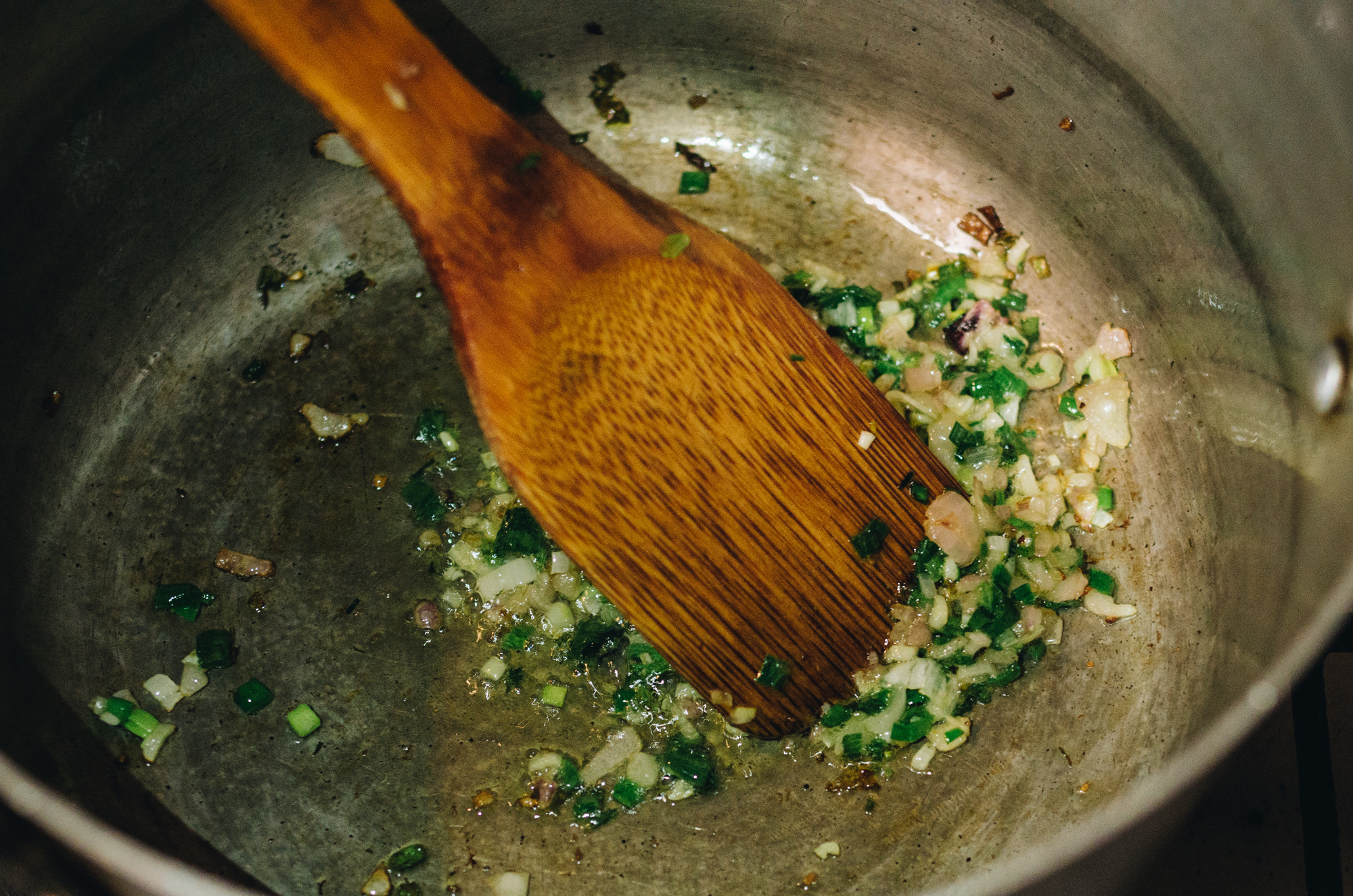 A close up of garlic being sauted in a pan with a wooden spoon