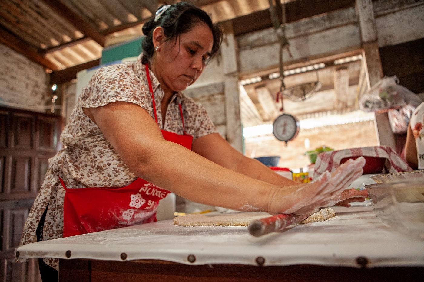 A Bolivian woman in a red apron rolls out dough