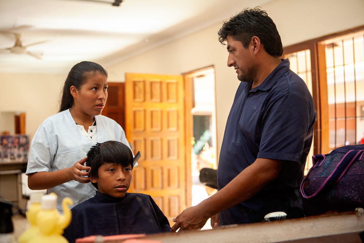 A woman cuts a young boy's hair while an instructor stands by