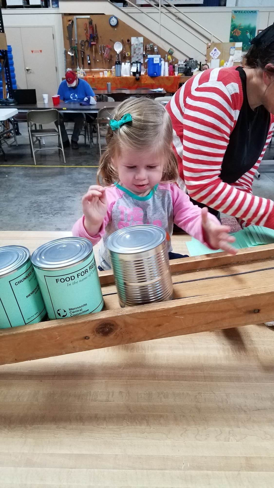 A young girl pushes cans down a wooden conveyer