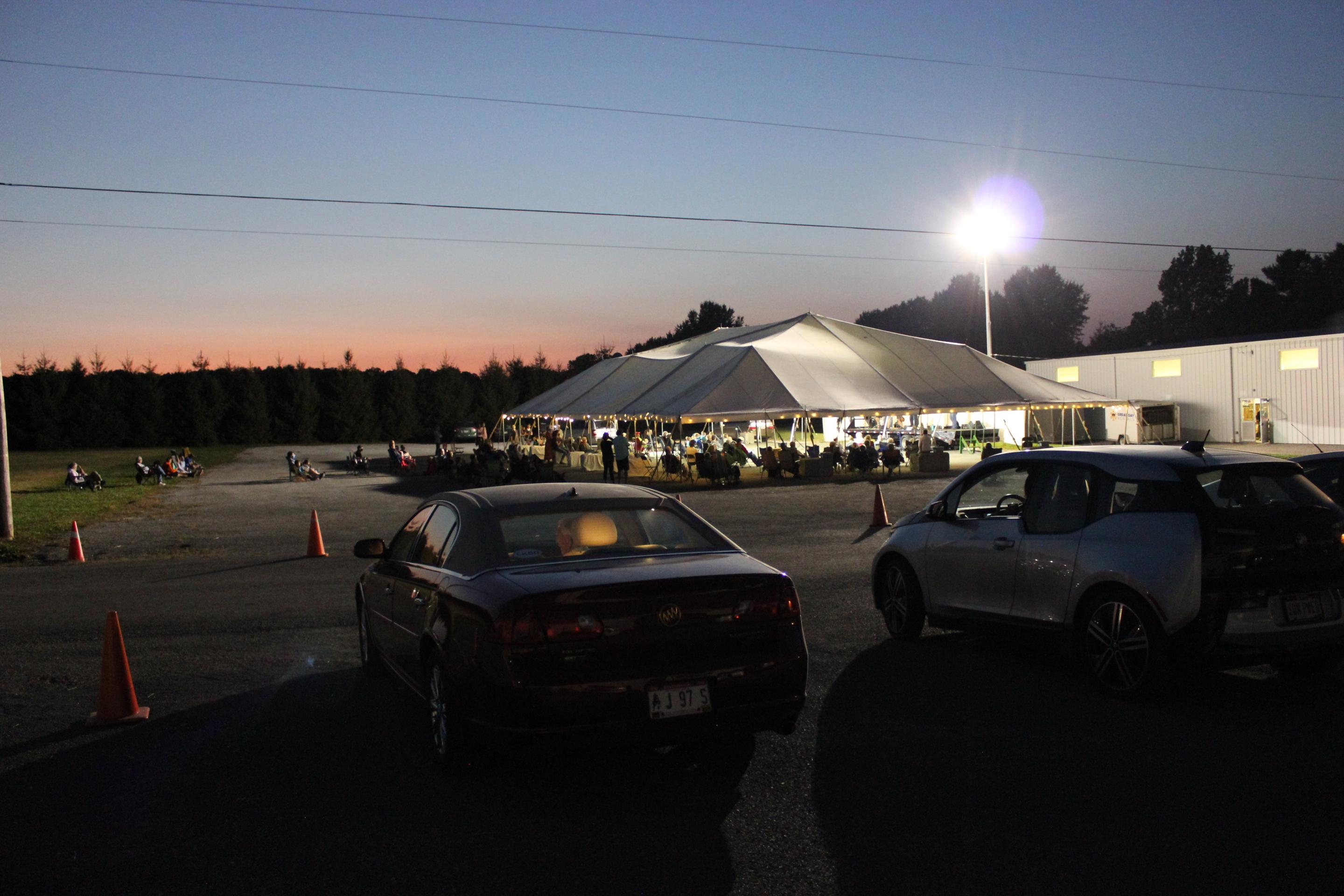 Cars parked outside of a large tent at sundown