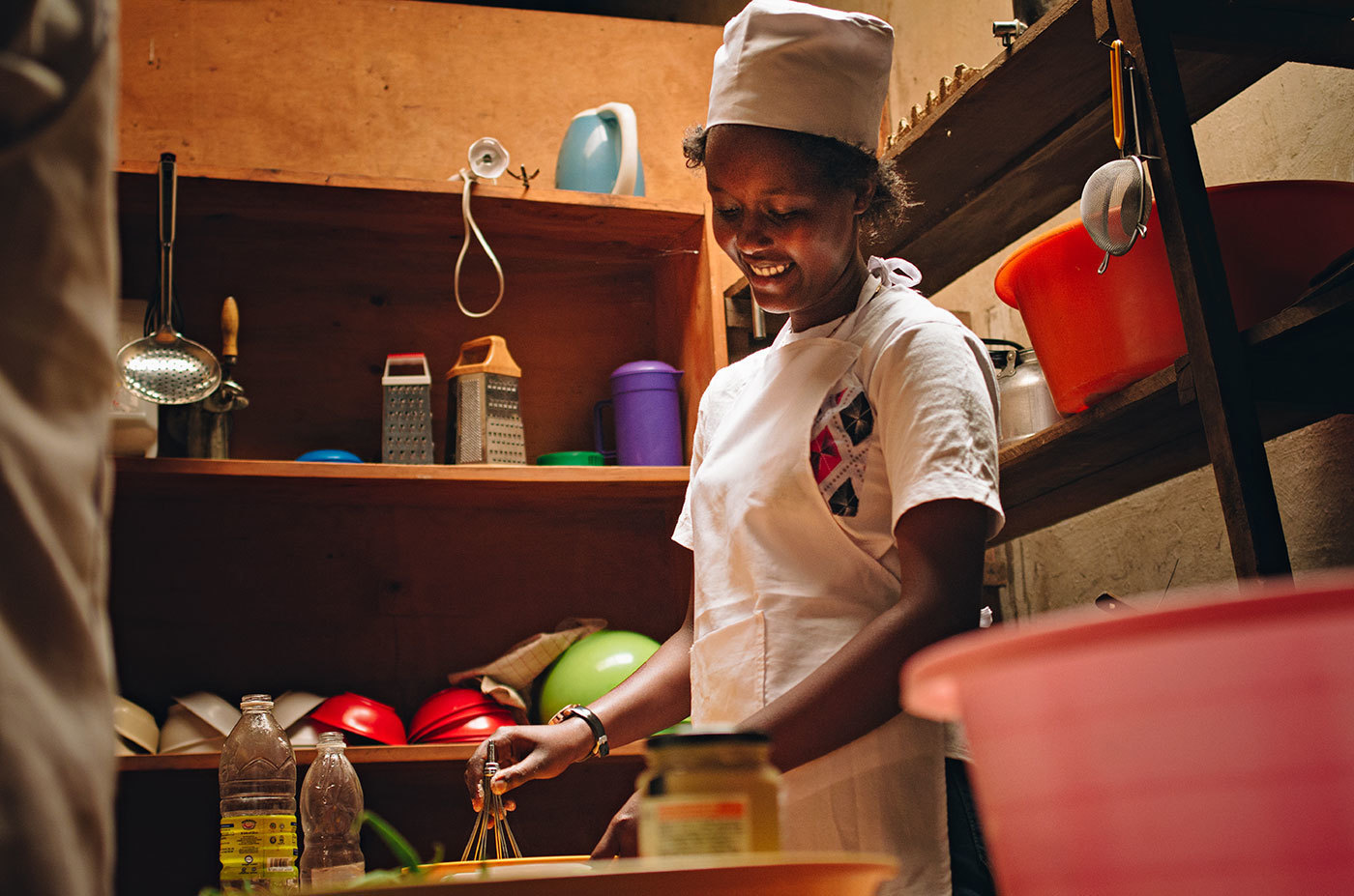 A Rwandan woman in a chef hat whisks something in a bowl