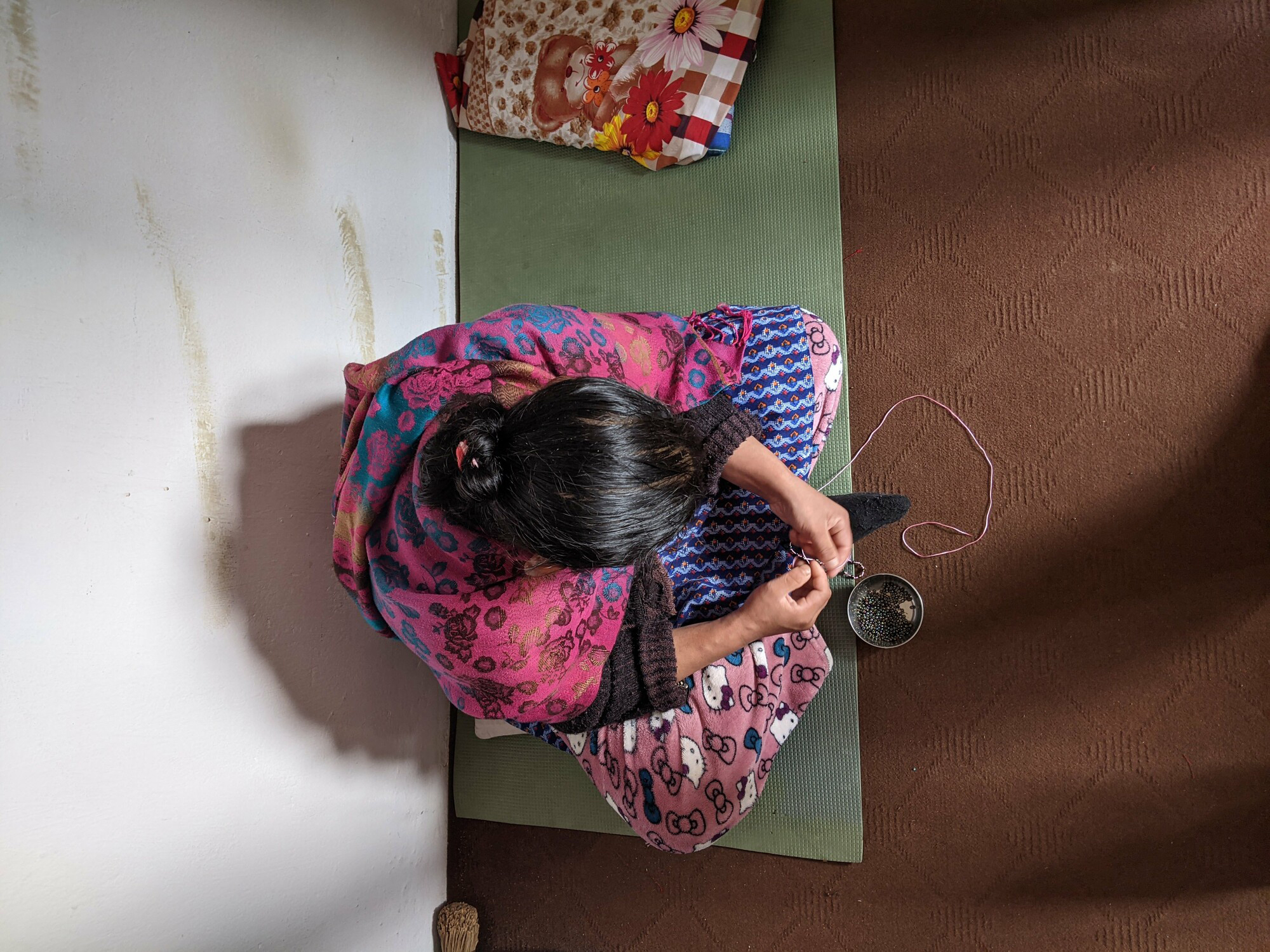 A woman sitting on a floor beading a necklace.