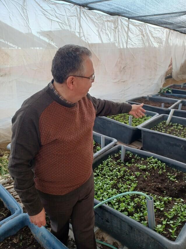 A man stands in a makeshift green house. He is jesturing to raised beds