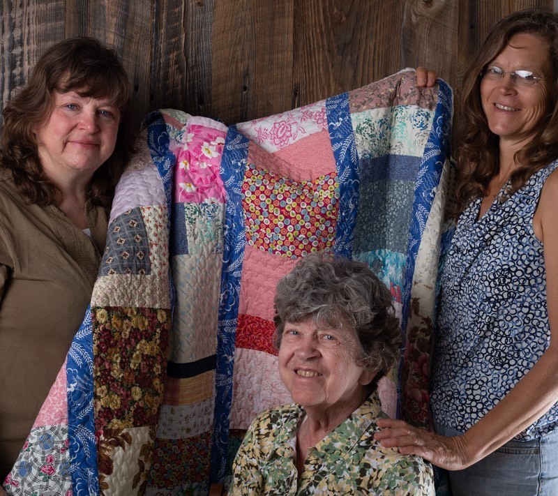 Three women pose with a quilt