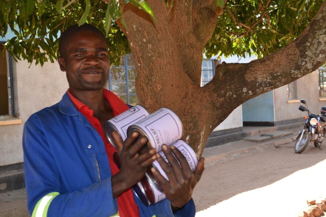A man in Zambia stands and holds large tin cans