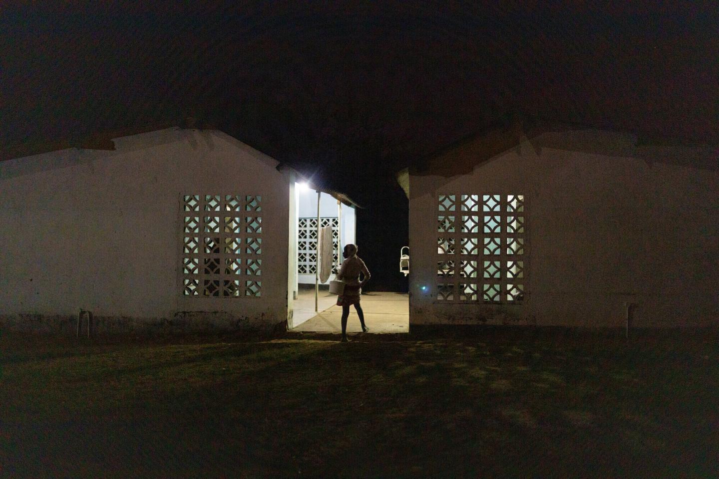 A person stands between two buildings. They are silhouetted by the lights coming from the buildings