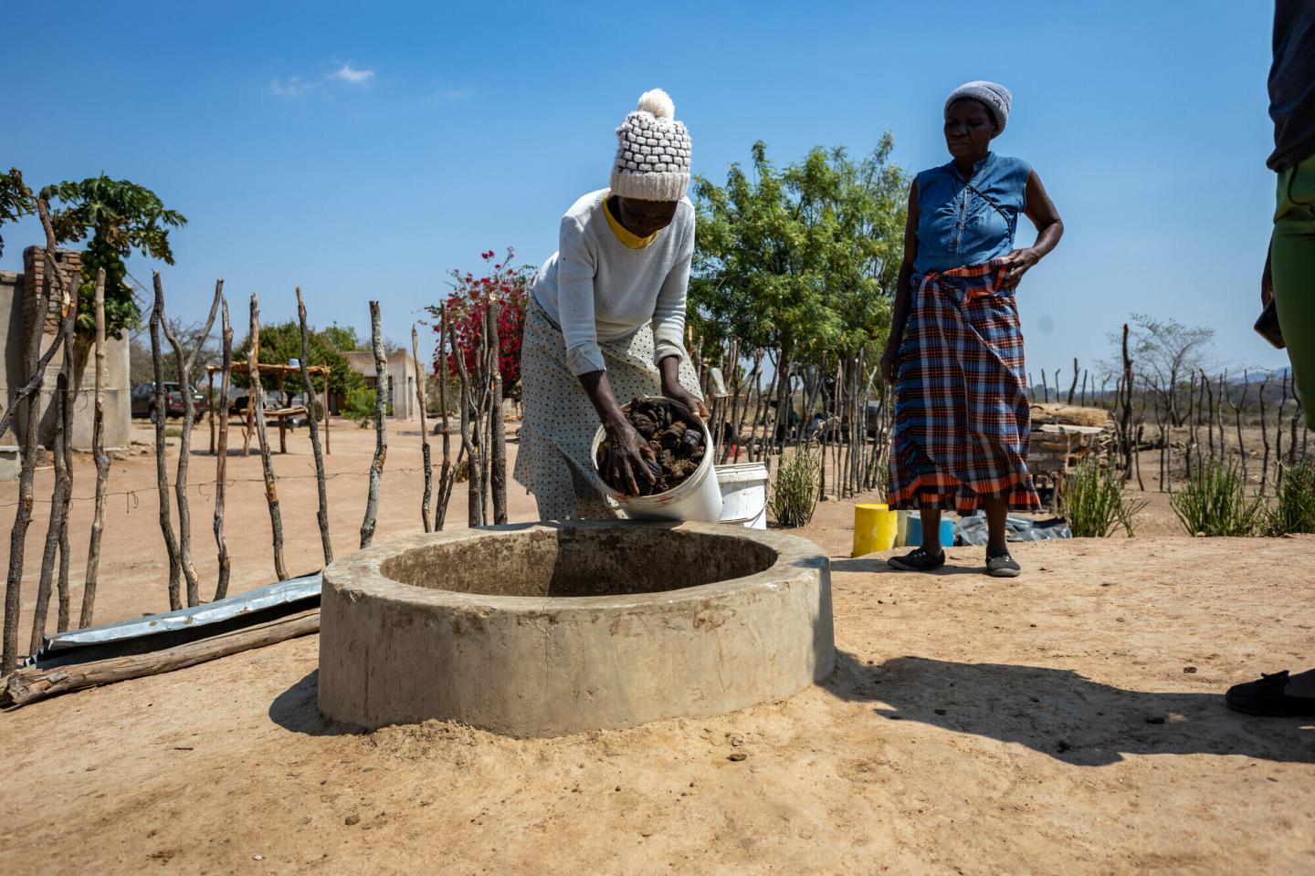A Zimbabwean woman dumps a bucket of manure into a round cement biodigester
