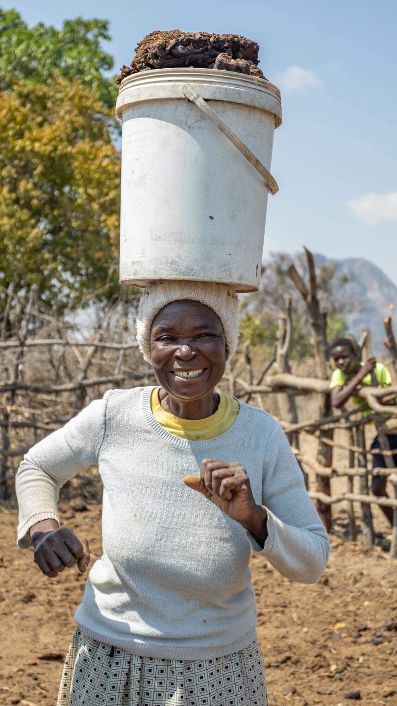 A Zimbabwean woman dances with a bucket of manure balancing on her head