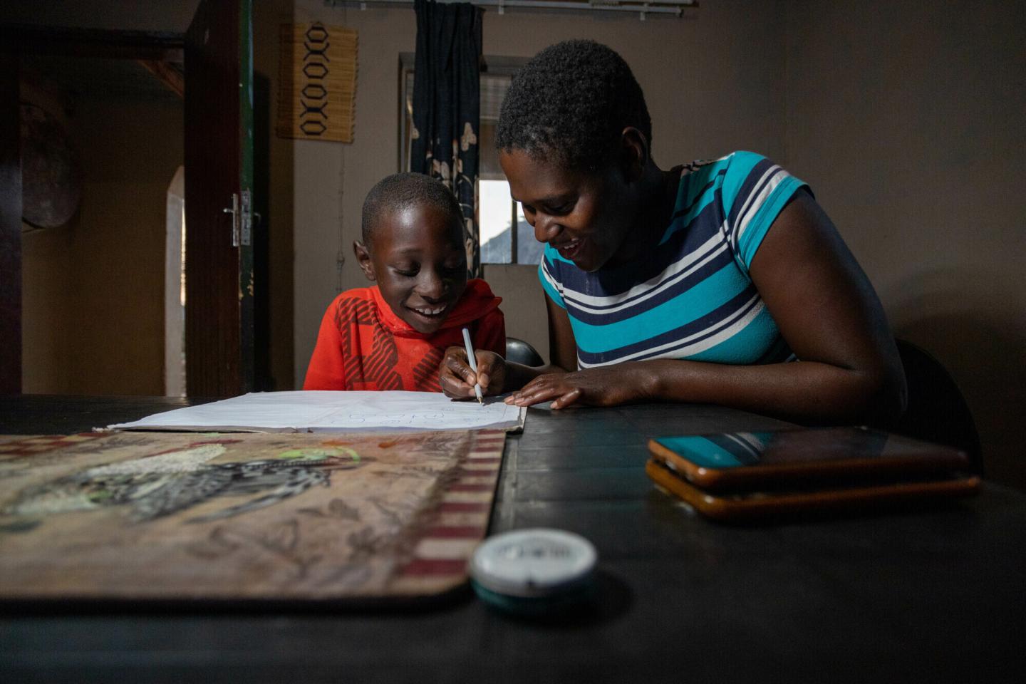 A mother helps her son with his homework at a table.