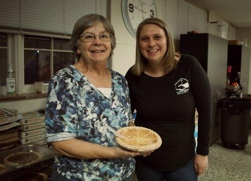 Two women stand together. One of them is holding a pie