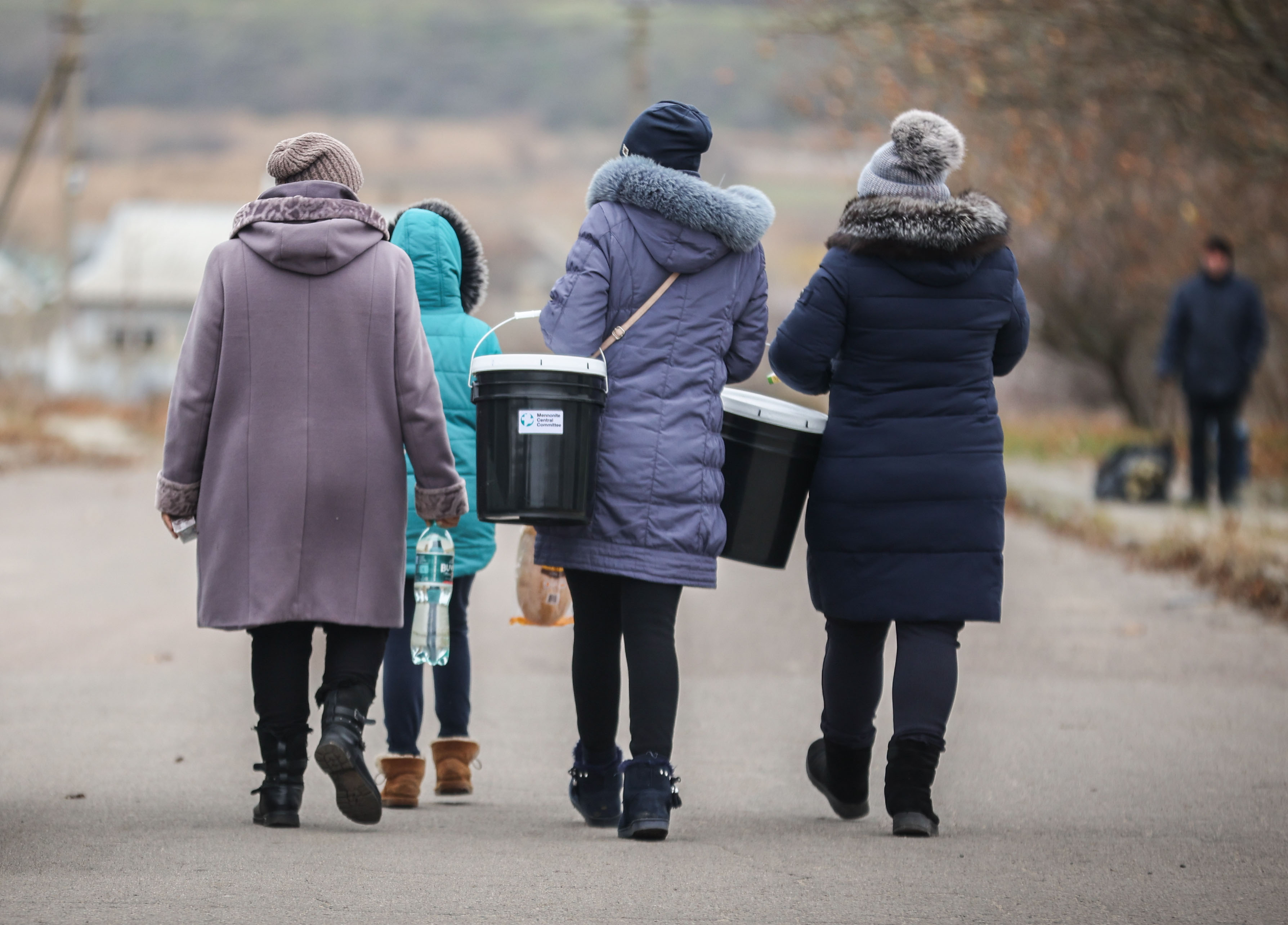 Four women walking down a road carrying MCC relief buckets.