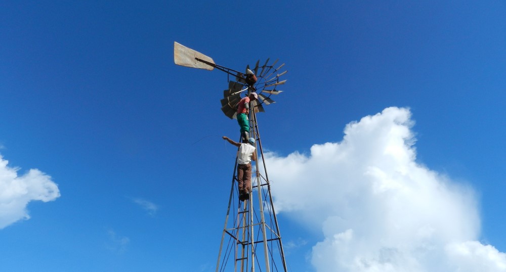 Three people climb on a wind-mill powered waterpump.