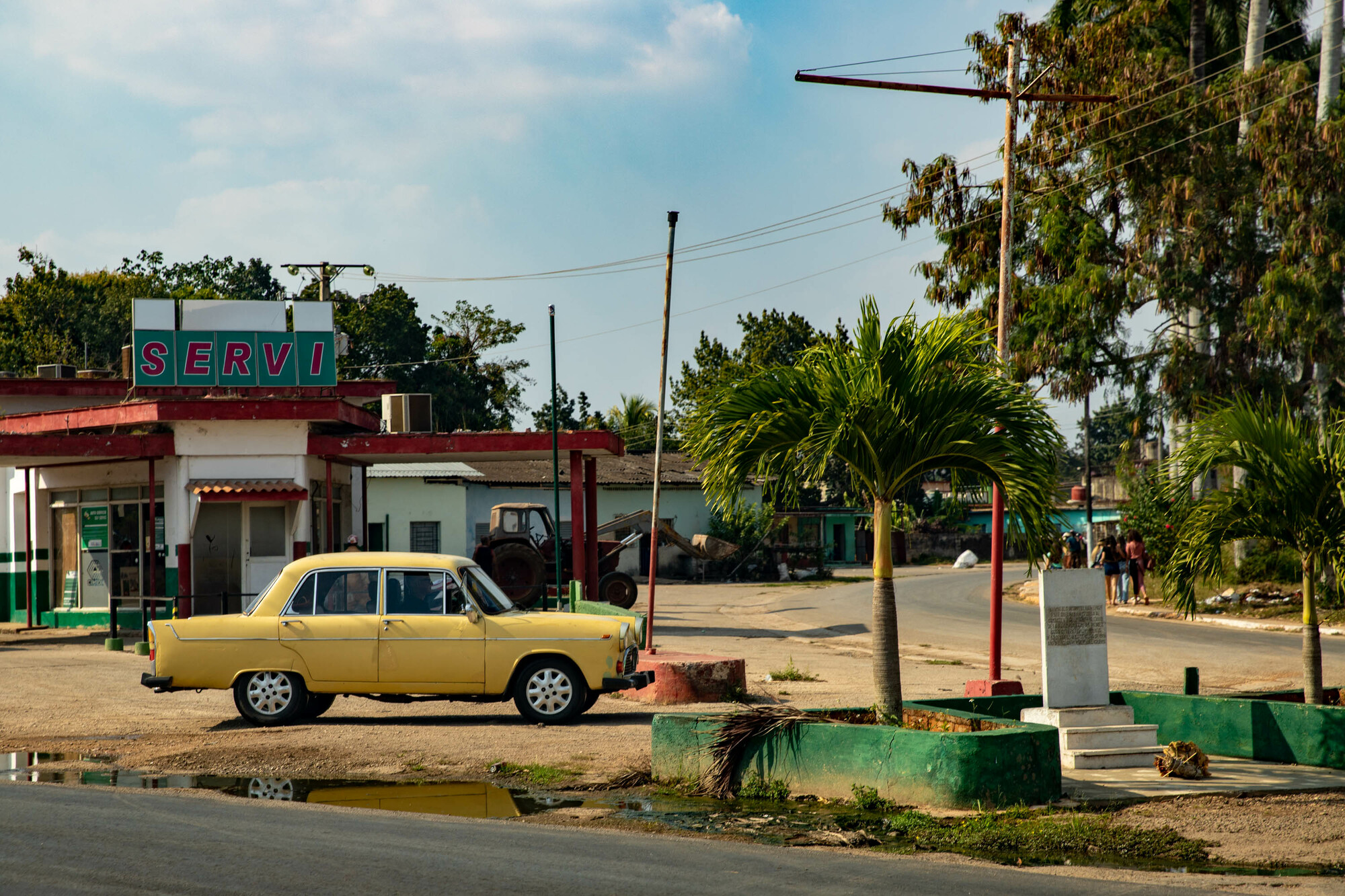 Old yellow car parked outside a dated gas station.