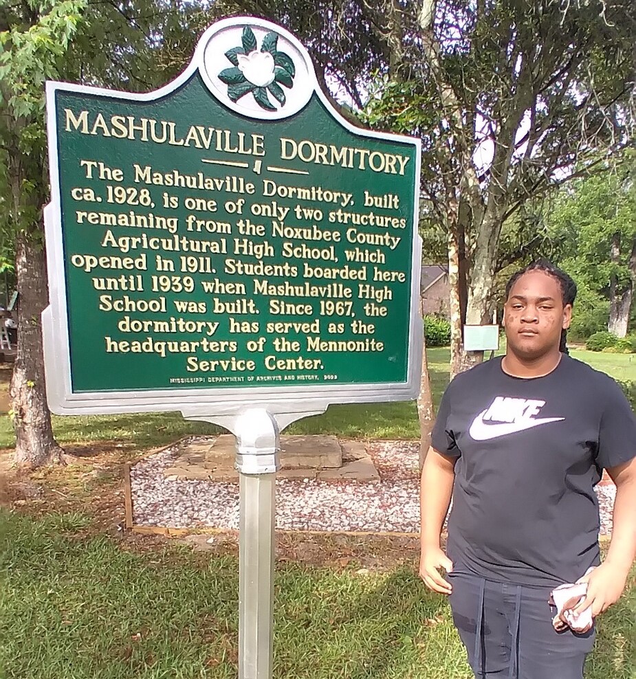 A young man standing next to a historical sign