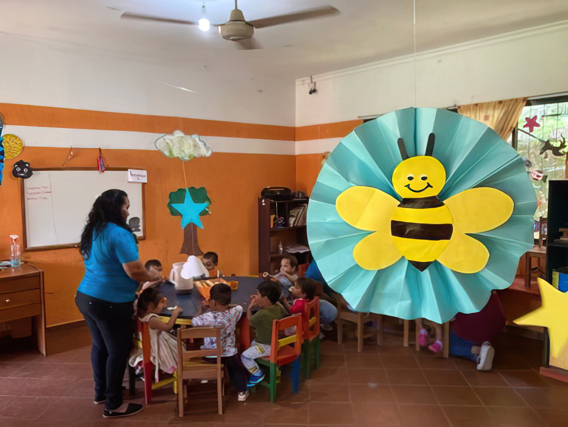 A woman standing in a room with a group of children sitting at a table