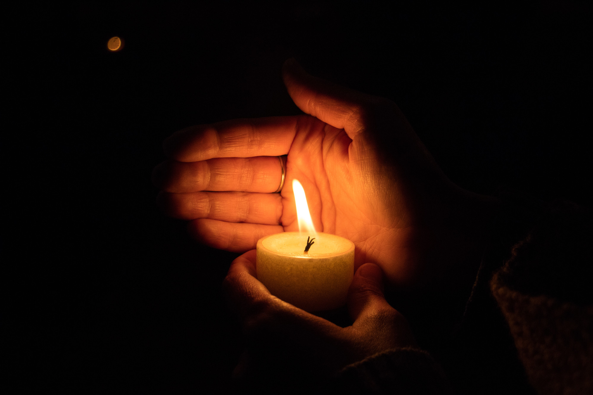 A hand shielding a lit candle from the wind with darkness all around.