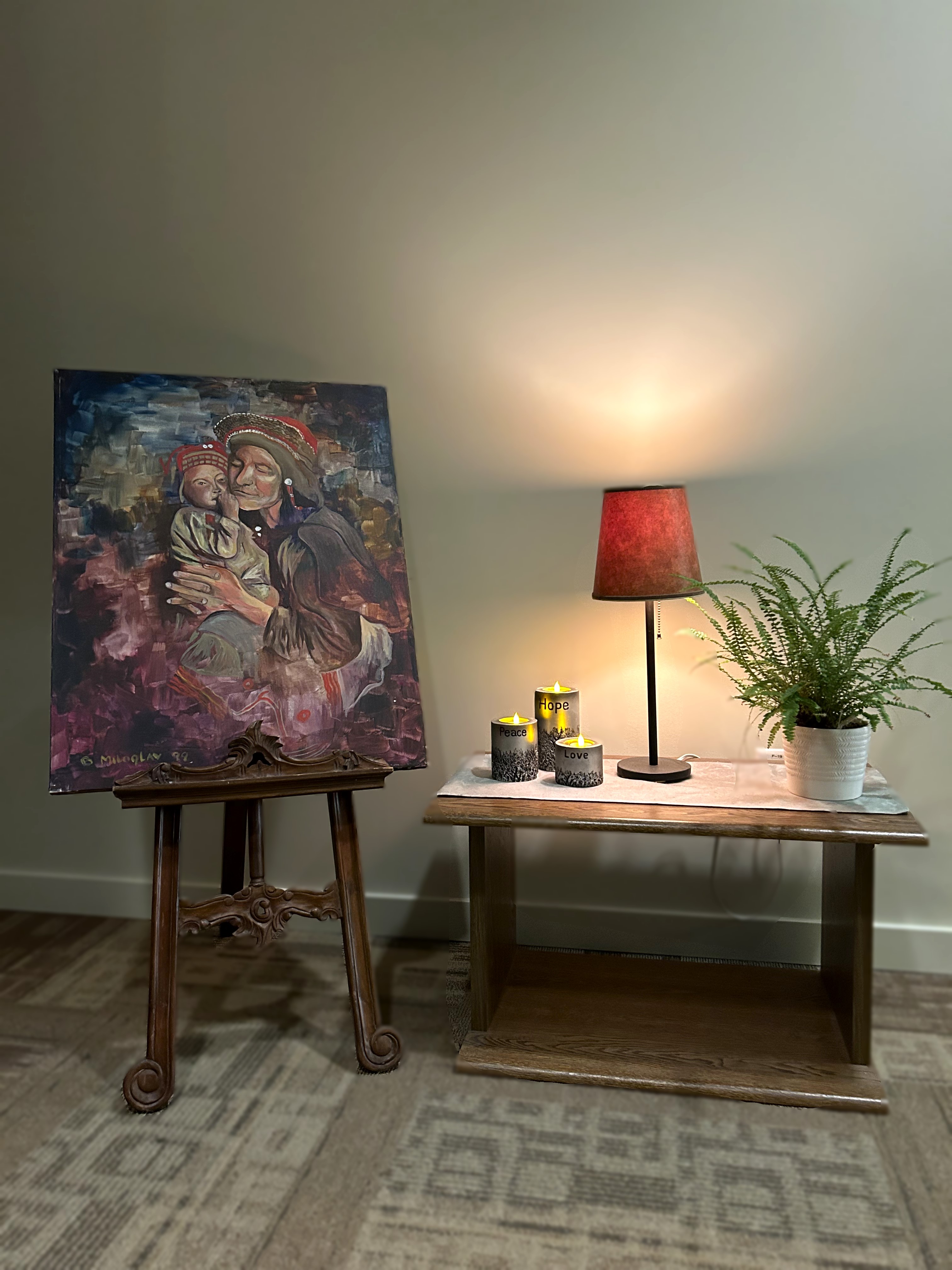 A display with art, a lamp, candles and flowers. The art is a picture of a mother holding a baby.