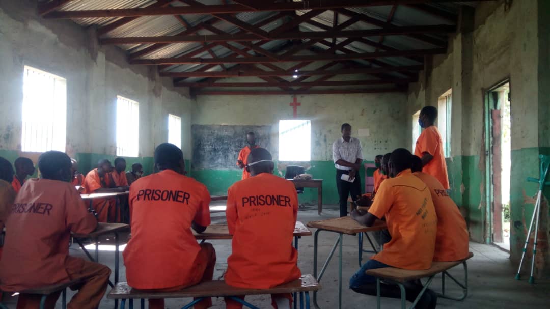 Incarcerated men gather in semi circle sitting at tables.