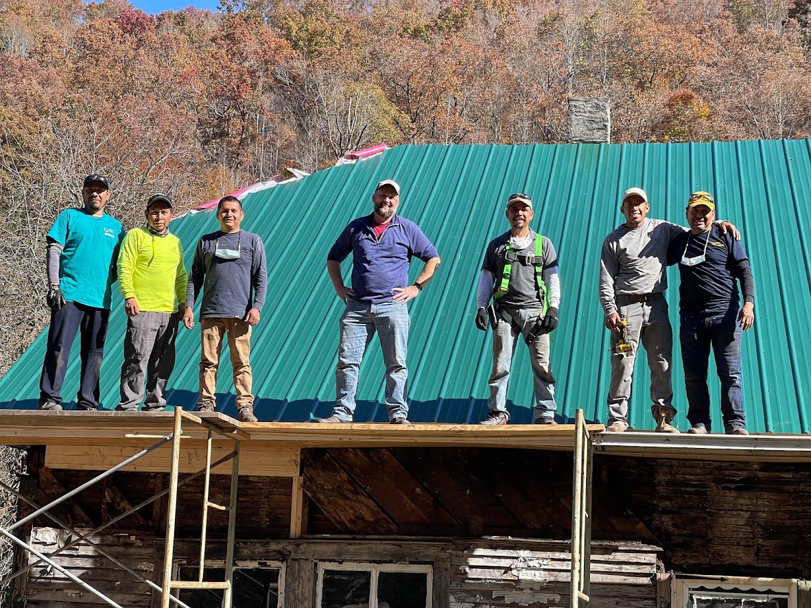 group of men stand on top of house with new metal roof