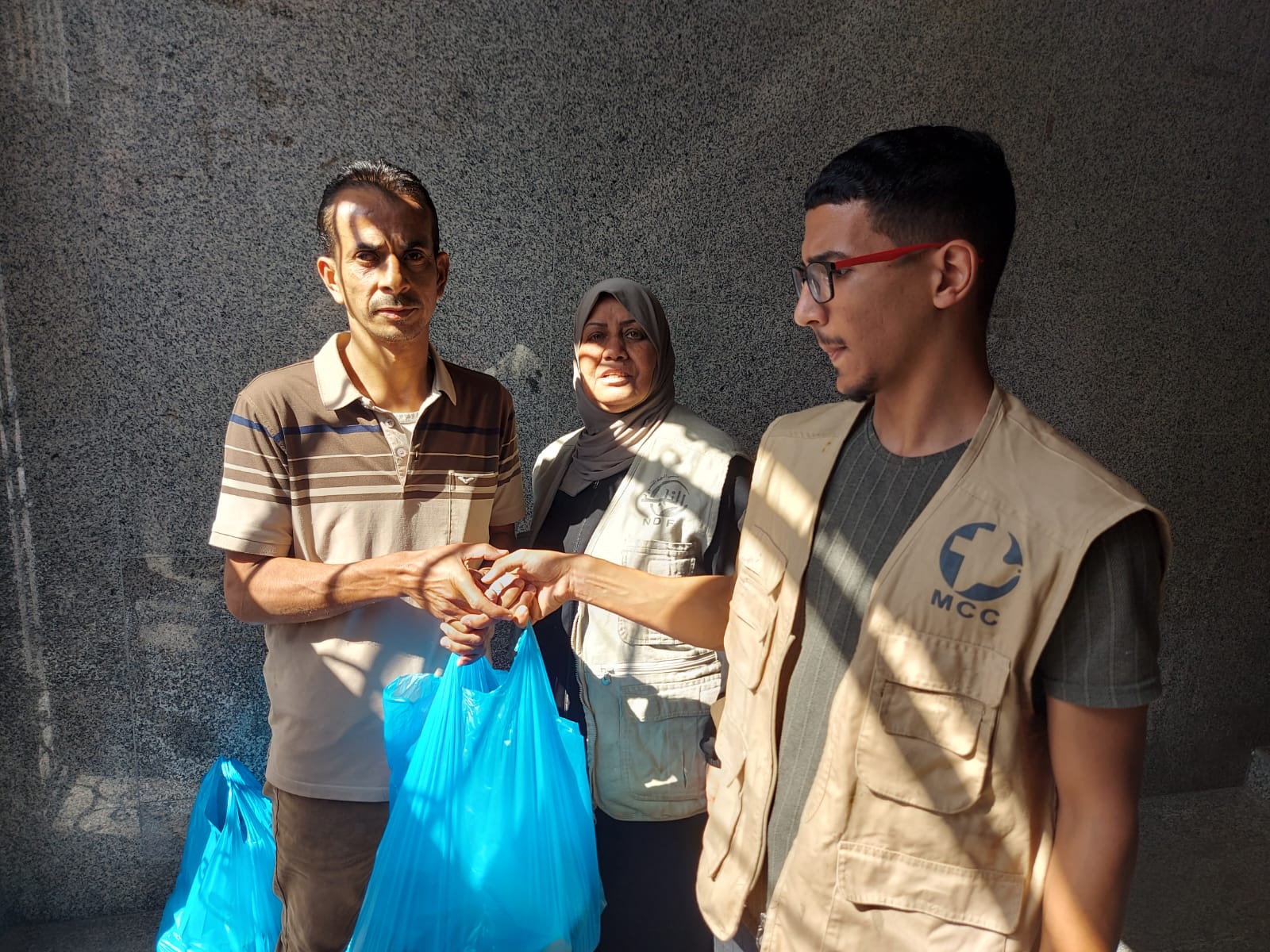 Two people hand a bag of supplies to a third person