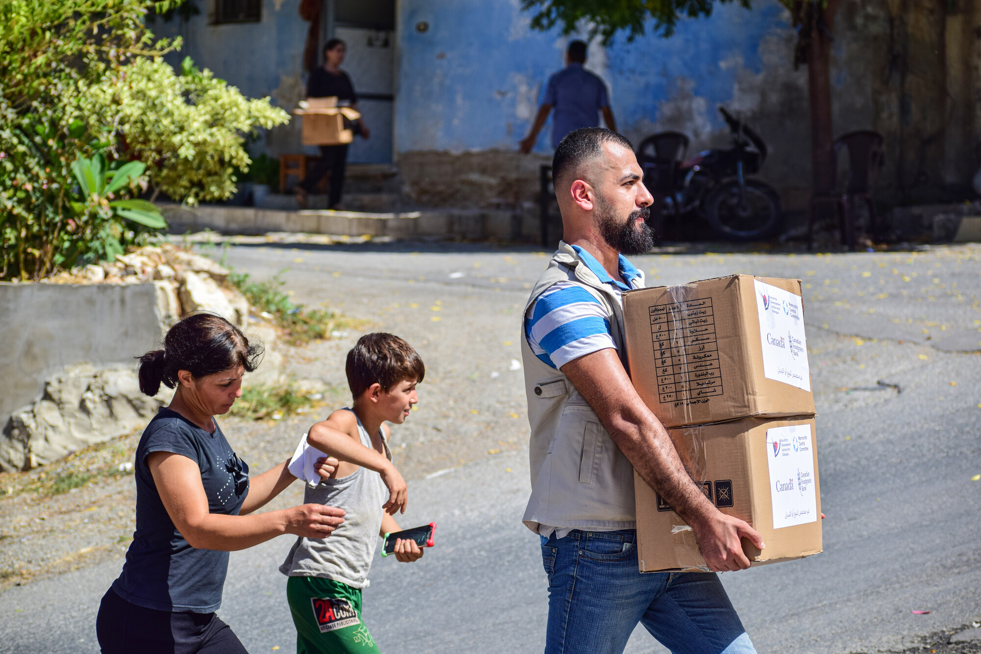 A man carries two boxes of aid as a woman and child follow him
