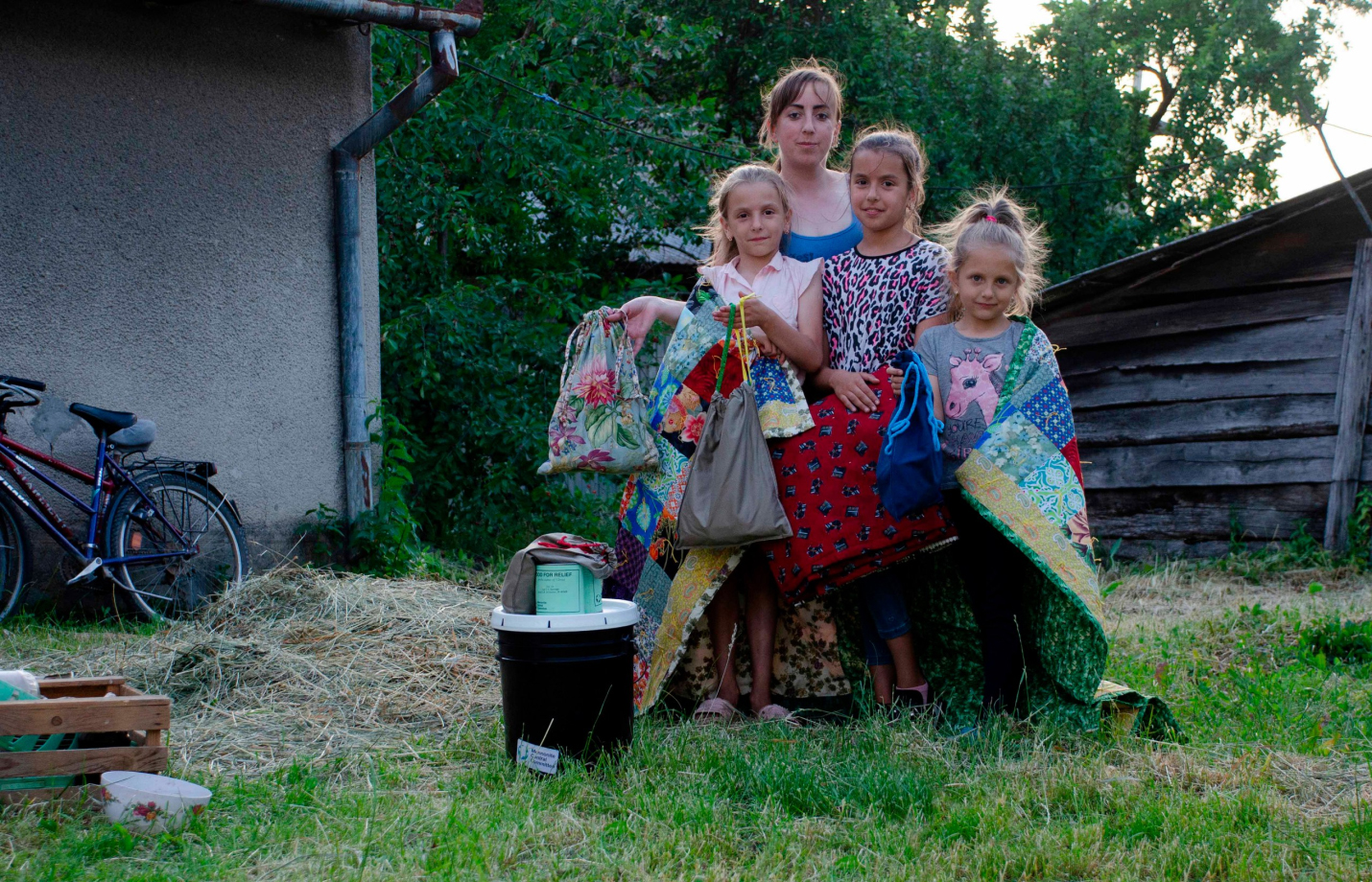 A picture of Marina* and her daughters are pictured with handmade comforters, hygiene items, relief kit and cans of meat supplied by MCC.
