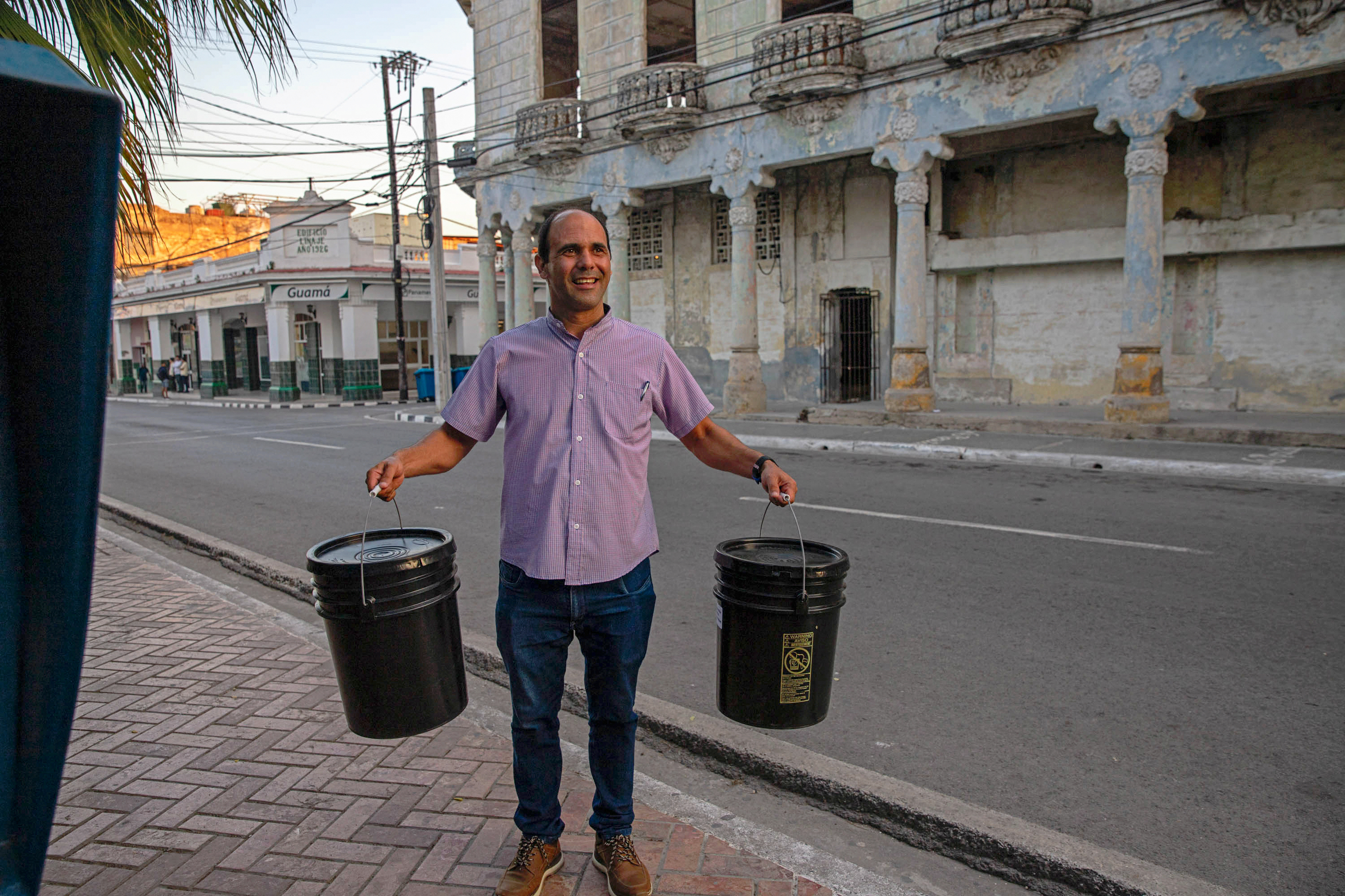 A man from Cuba holds two relief kits on a sidewalk. 