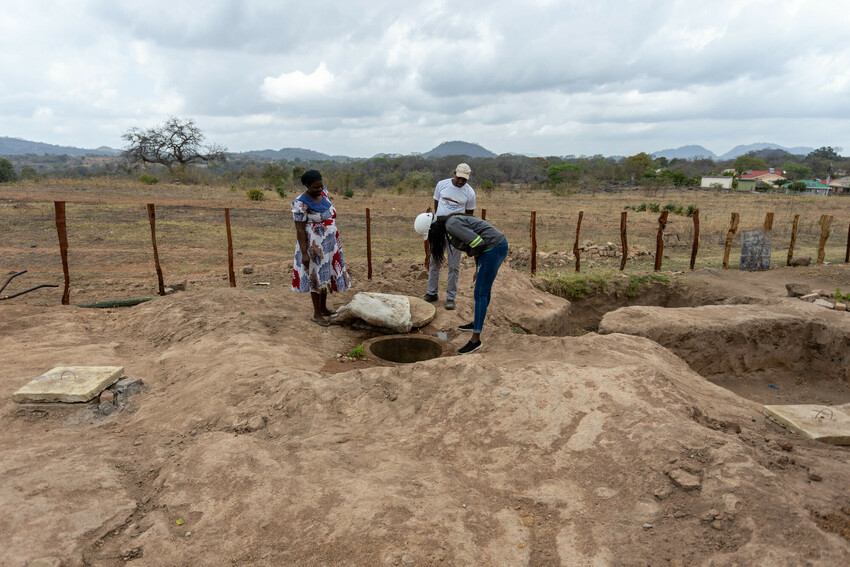 A group of three people looking into a dug hole in the ground
