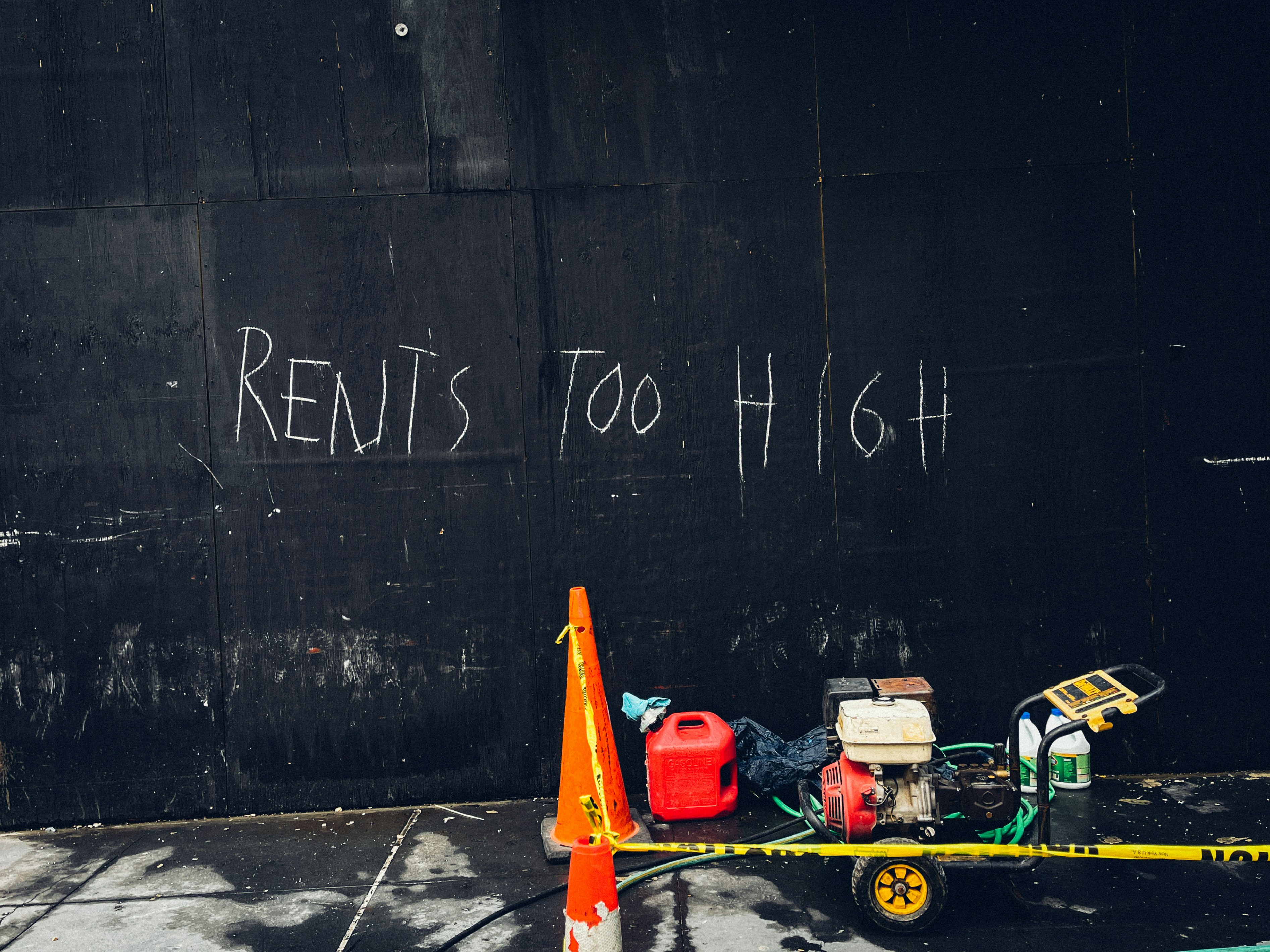 black painted wall with words "rents too high" written with white chaulk