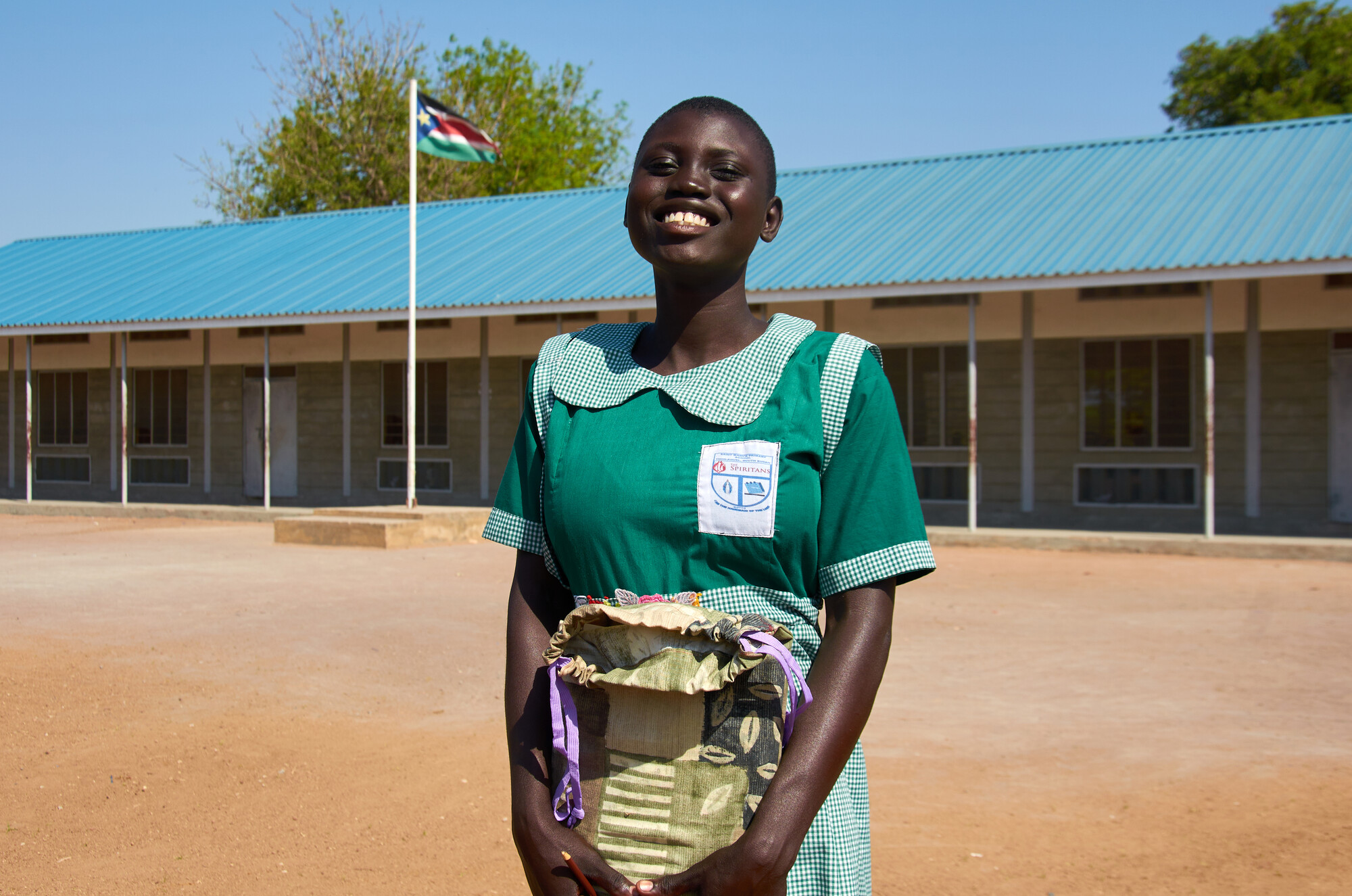 A girl standing outside of a school holding a school kit