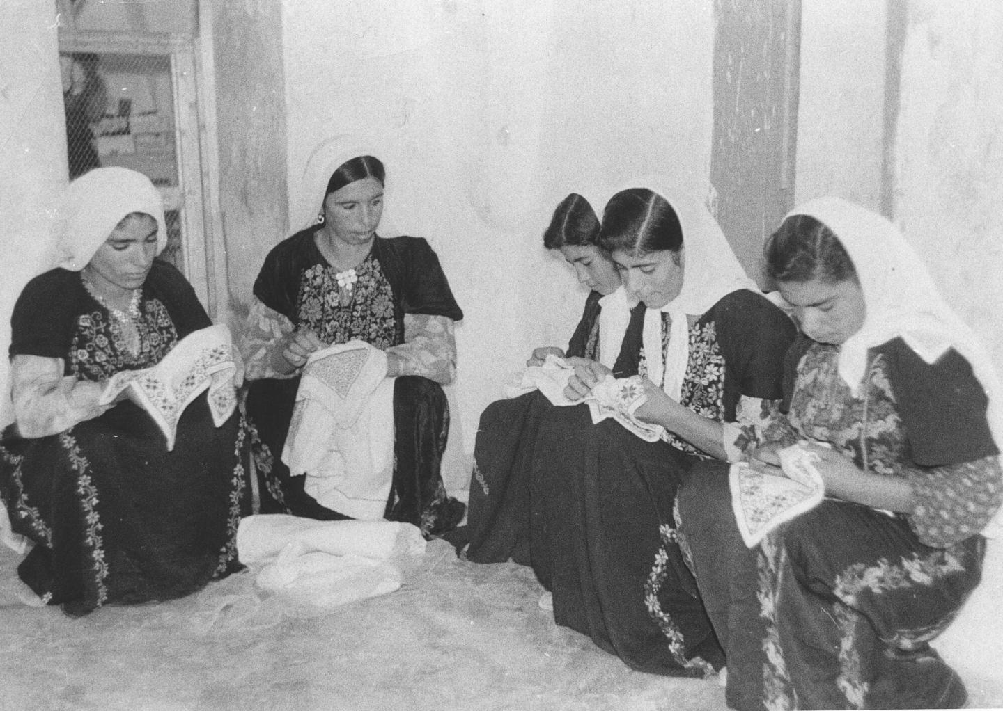 A black and white photo of five Palestinian women sewing together