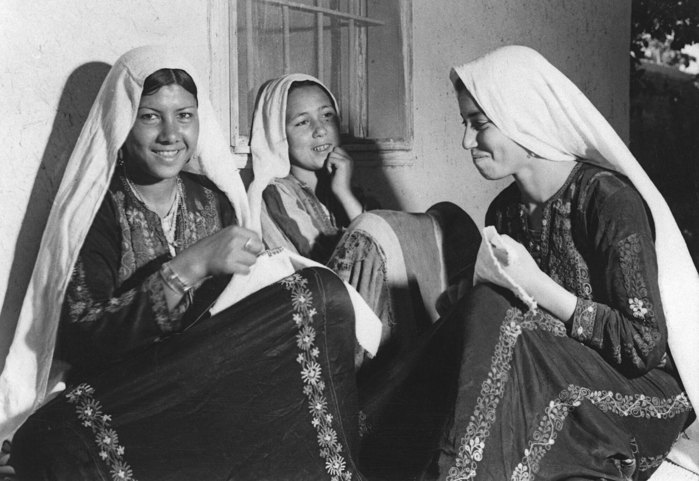 A black and white photo of three Palestinian girls sewing together
