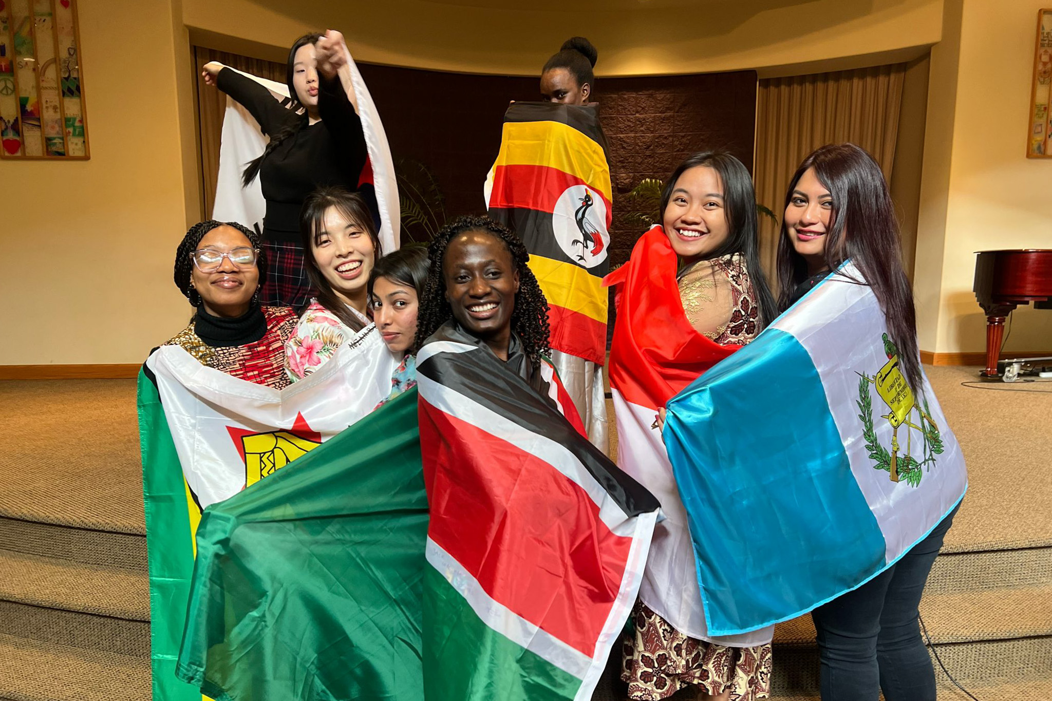 A group of smiling young adults stand posed while wrapped in flags from various nations.
