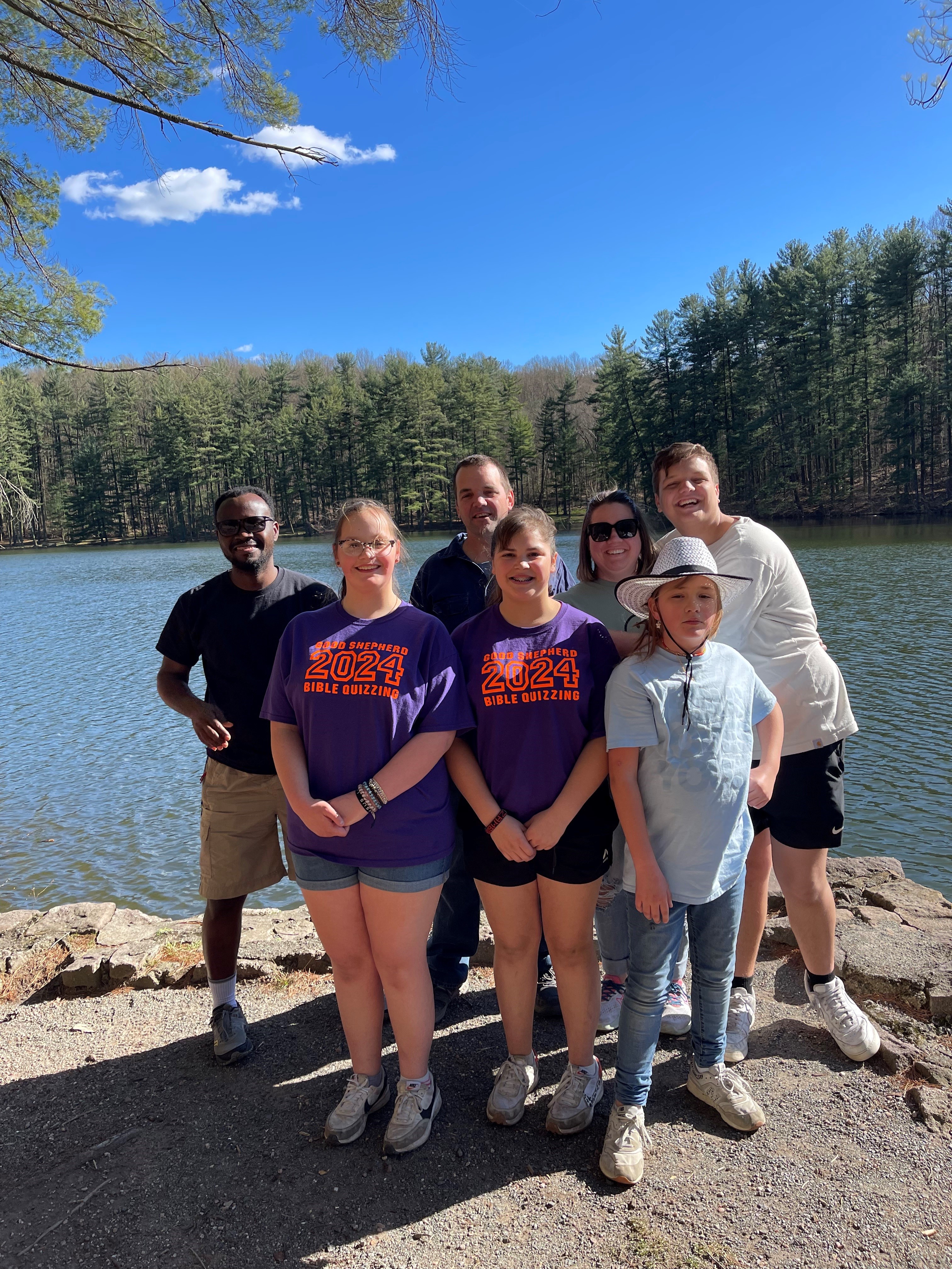 Family and IVEP participant stand in front of a wooded lake.