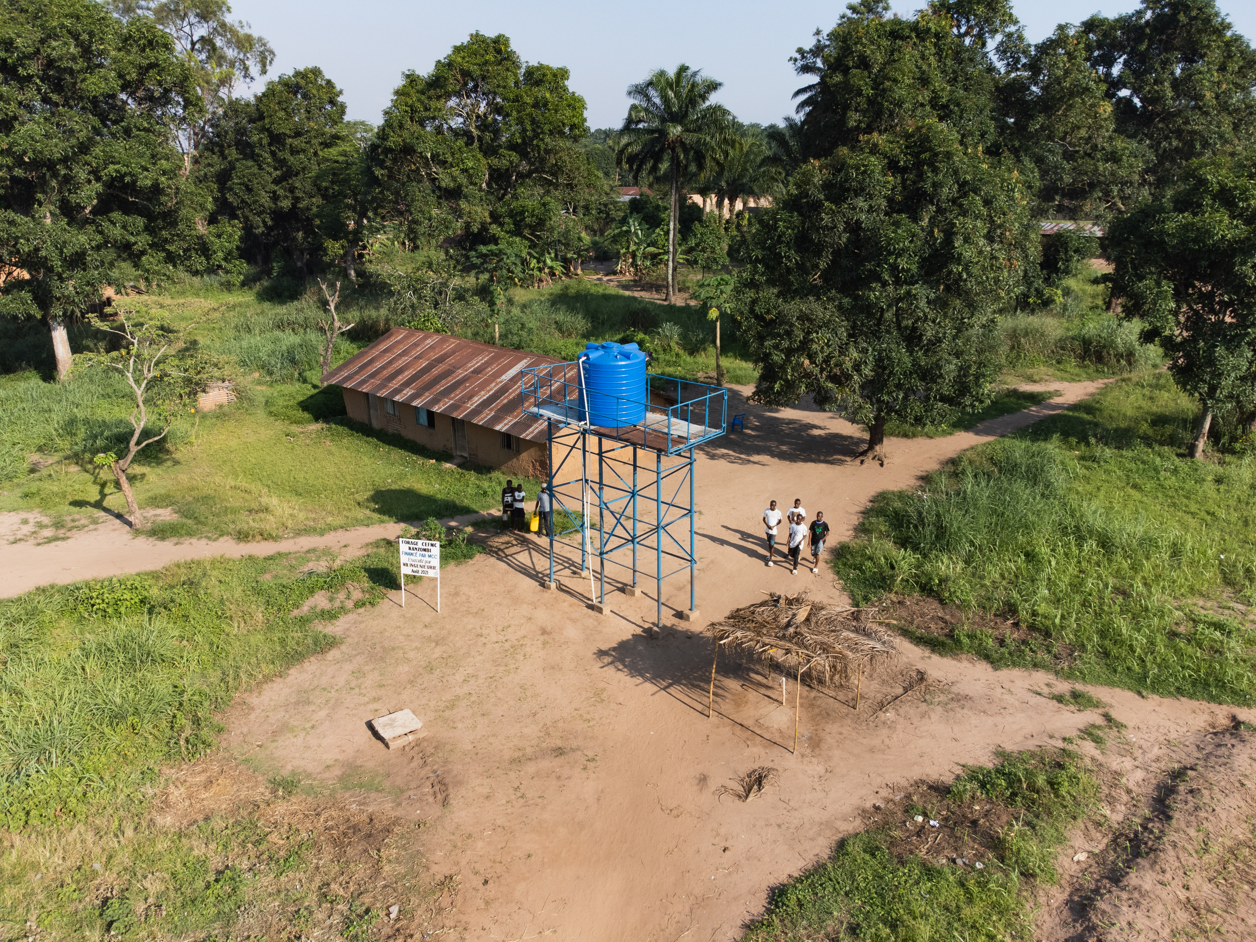 This borehole pictured shows all parts of the finished borehole after it is drilled. The Blue tank holds water that the pump pulls from the borehole. The spicket itself is underneath the shadded grass roof next to the blue tank tower. You can see by the paths leading to the borehole that it serves the community from all directions where people are coming for water here.