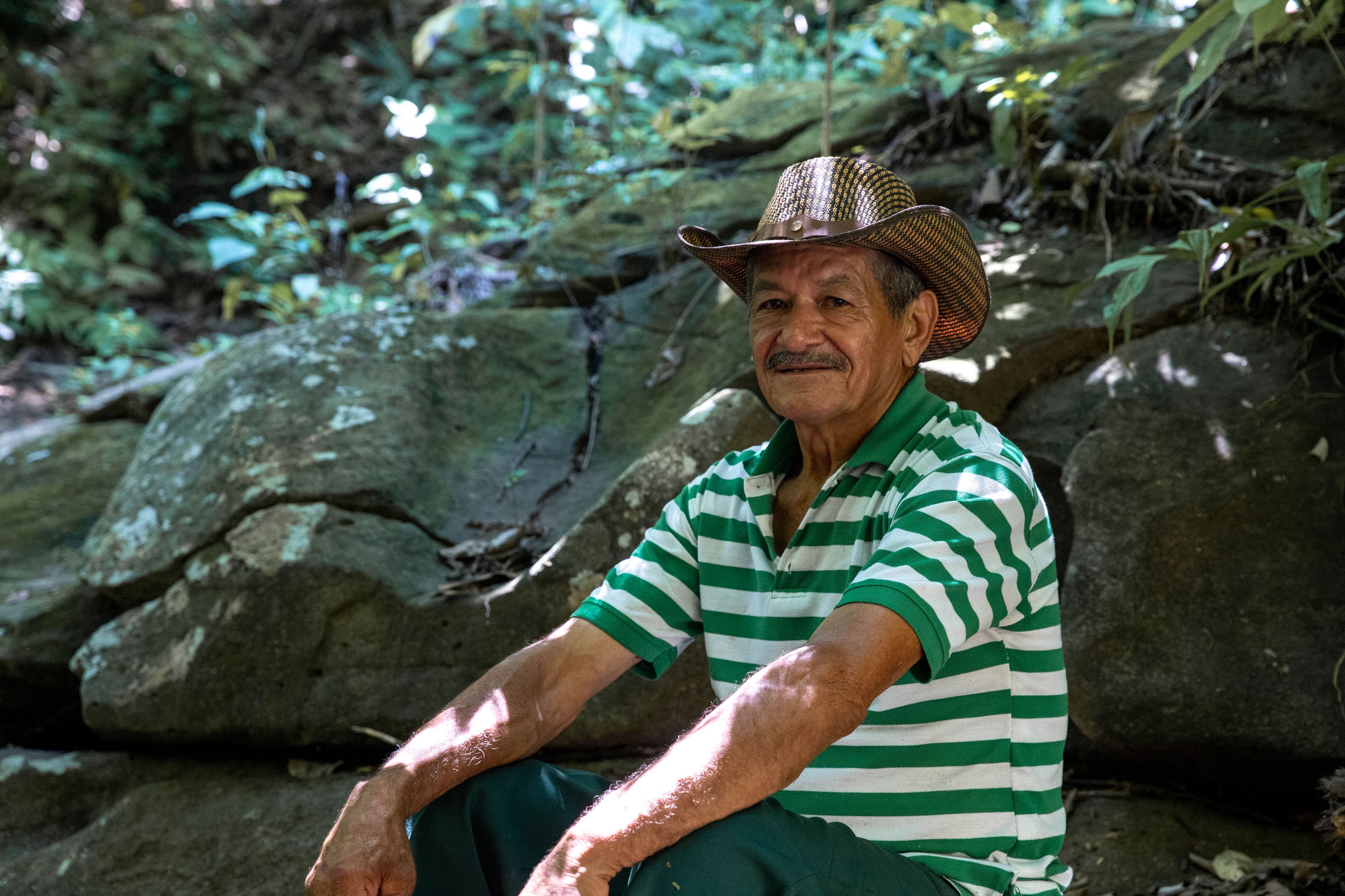 Eduardo Rodríguez poses for a portrait in a lush, shady spot next to a clear stream with a small waterfall that the community refers to as “Eden” for its paradisiacal qualities.