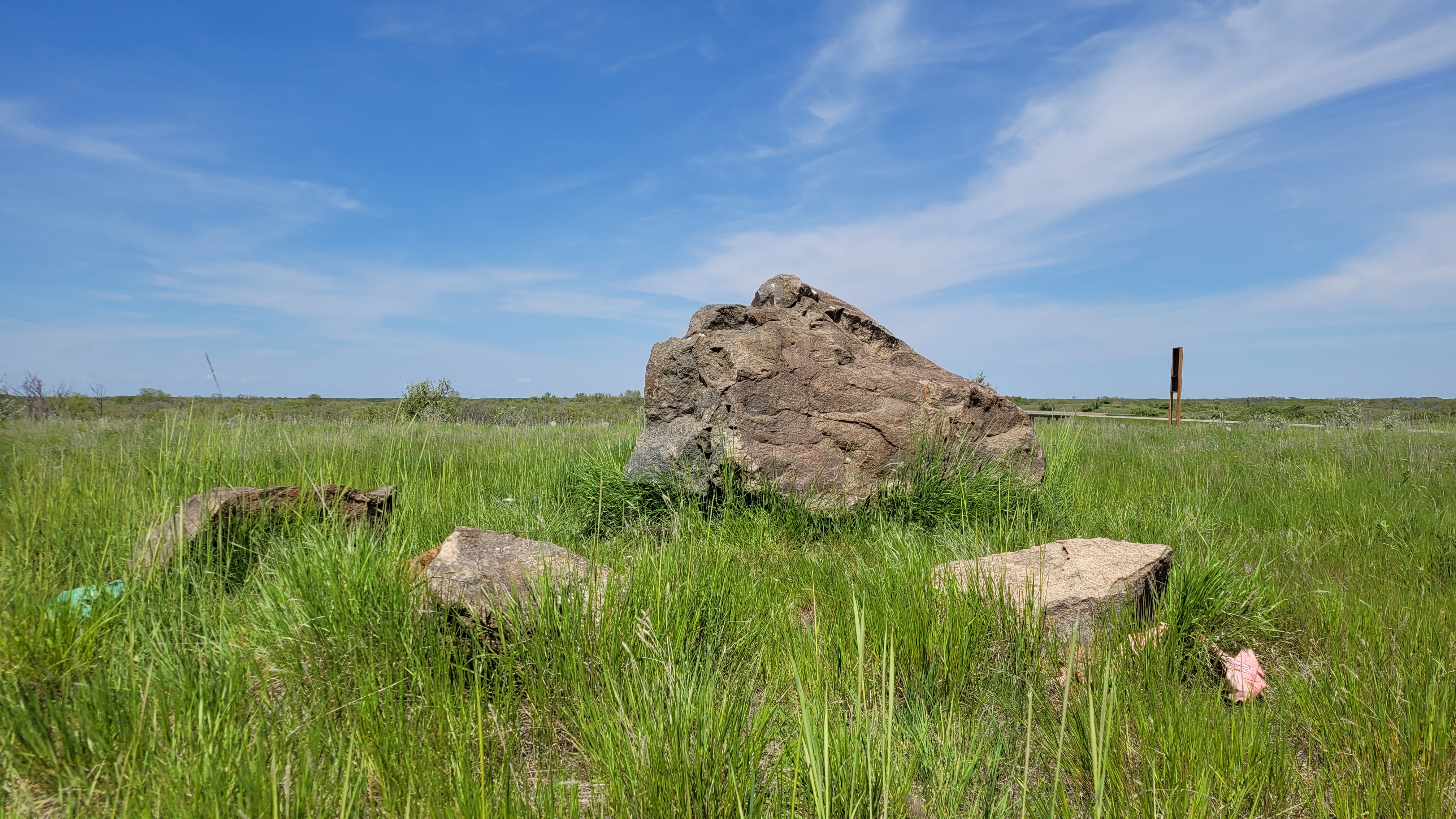 A large stone in a green, grassy field under a blue sky.