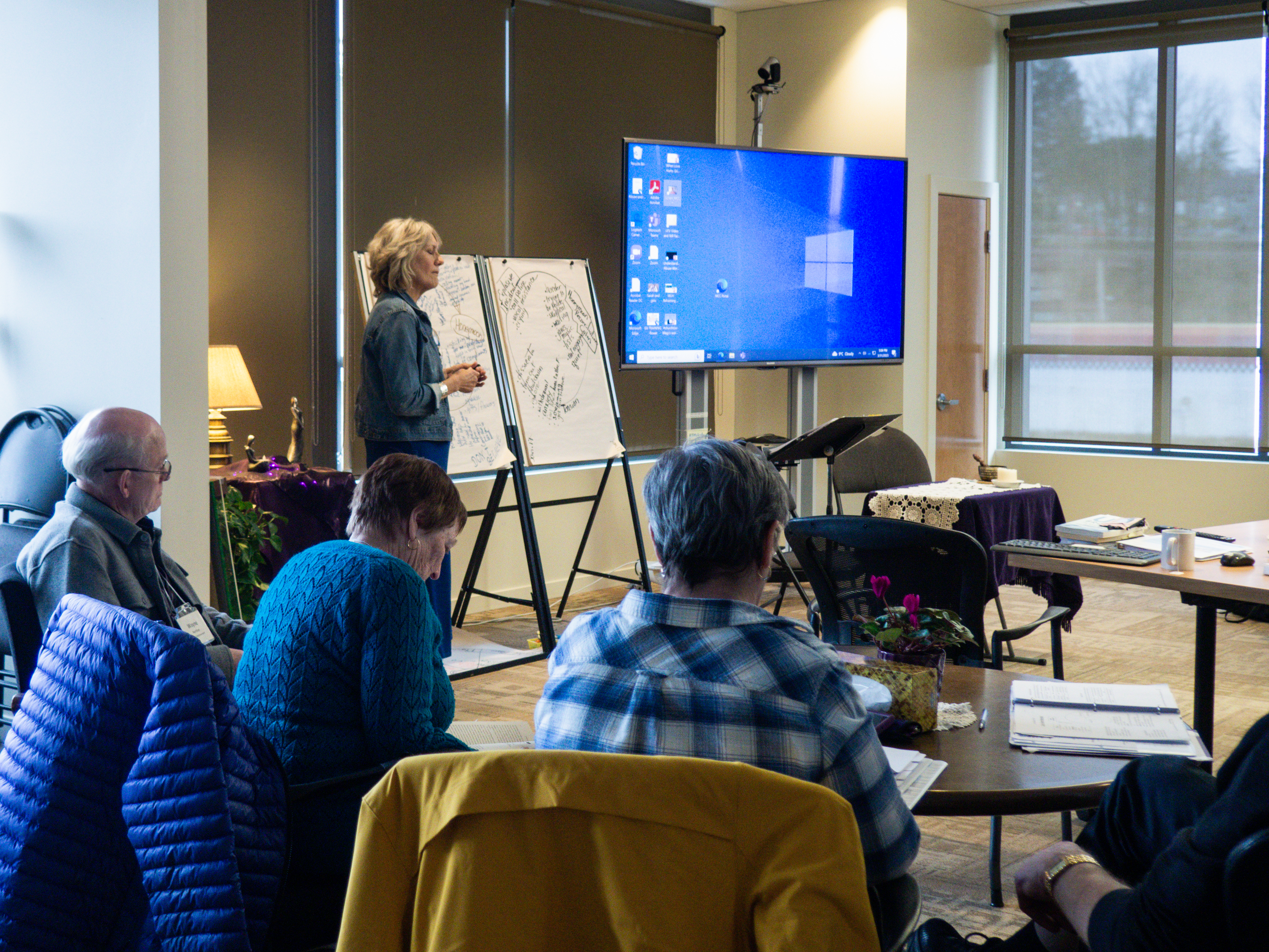 A woman facilitating a group workshop with a few participants pictured.