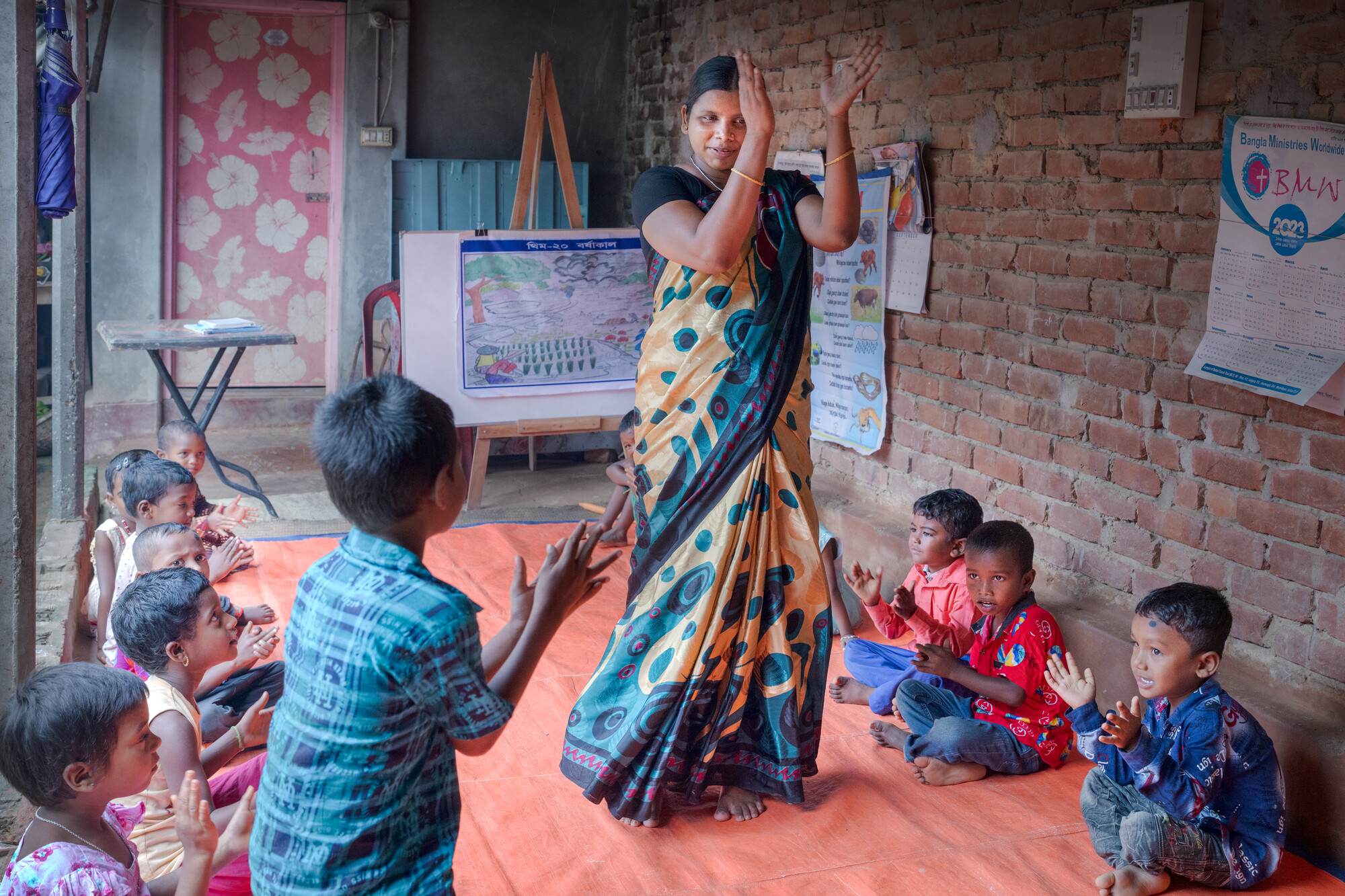 A person, surrounded by clapping children stands with her arms raised in a clapping motion.