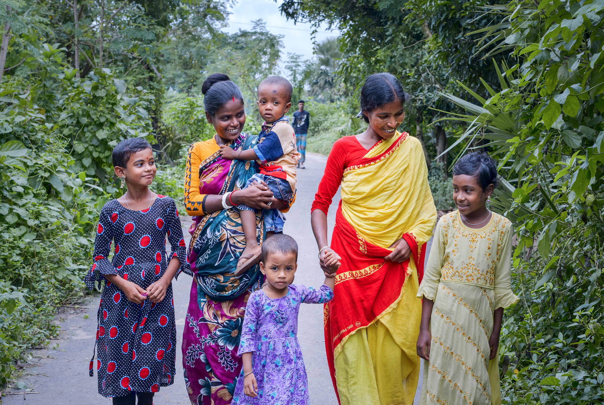 Two mothers walk with their four children down a path framed by green growth.