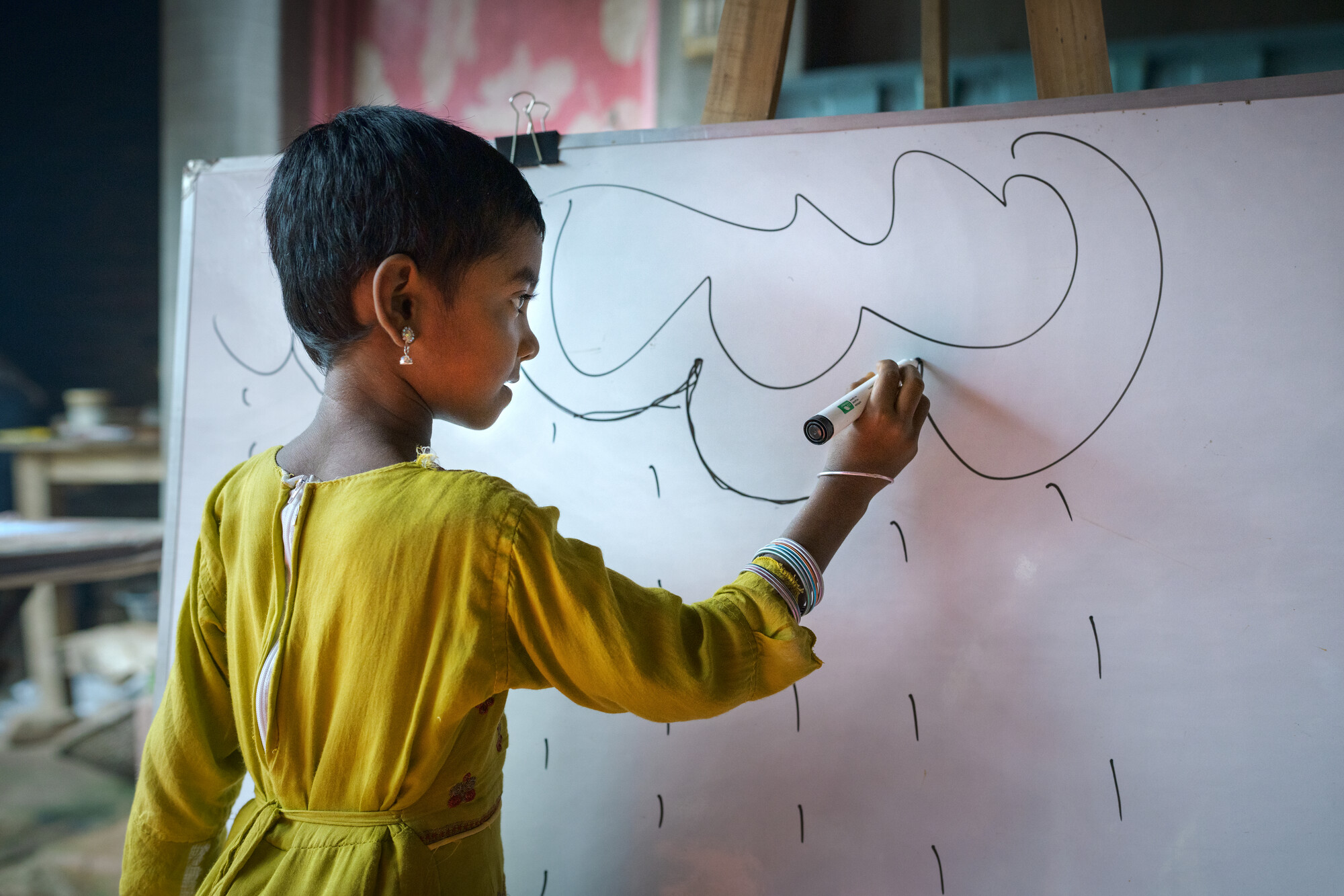 A child draws rain clouds on a whiteboard.