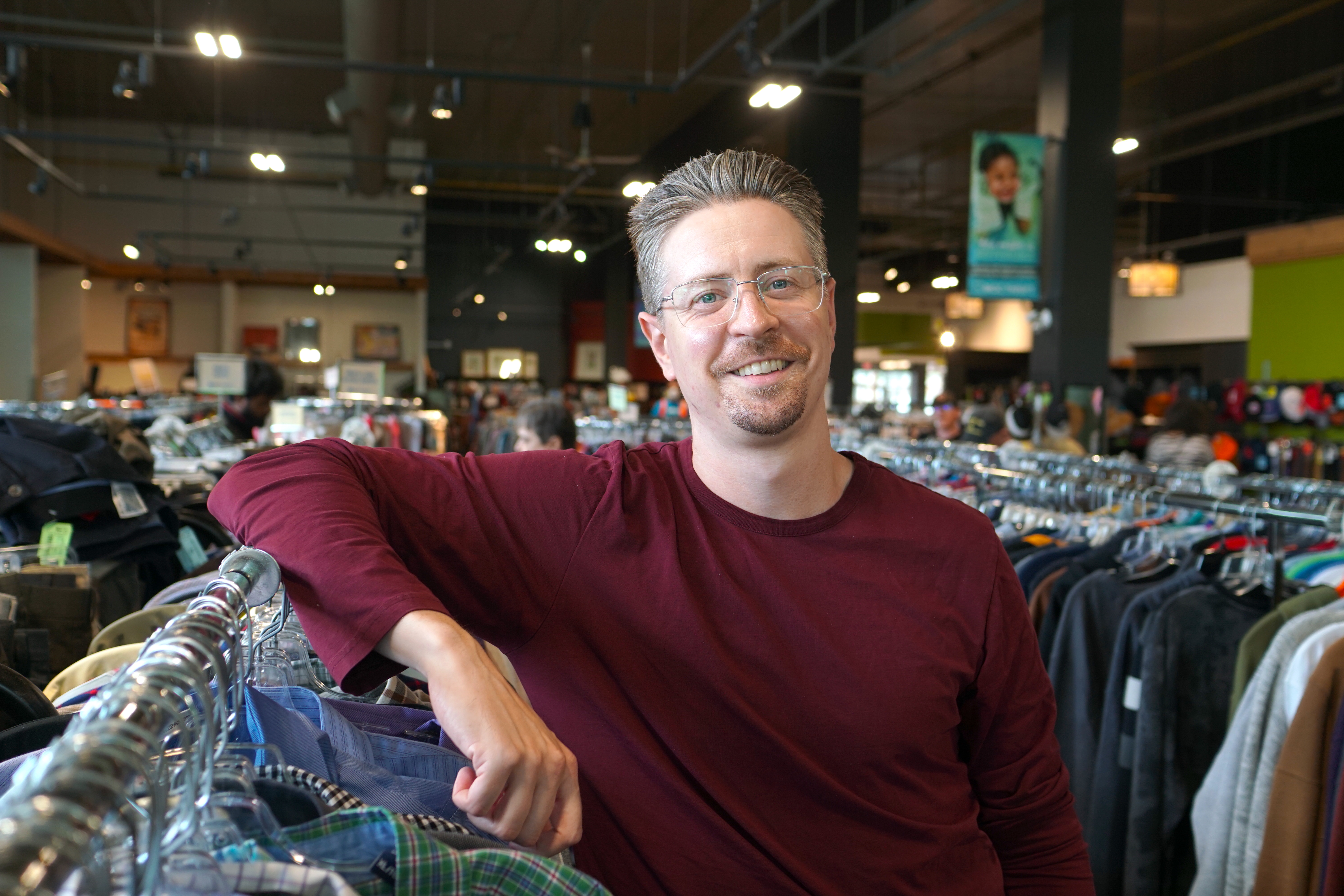 Smiling man leaning on clothing rack