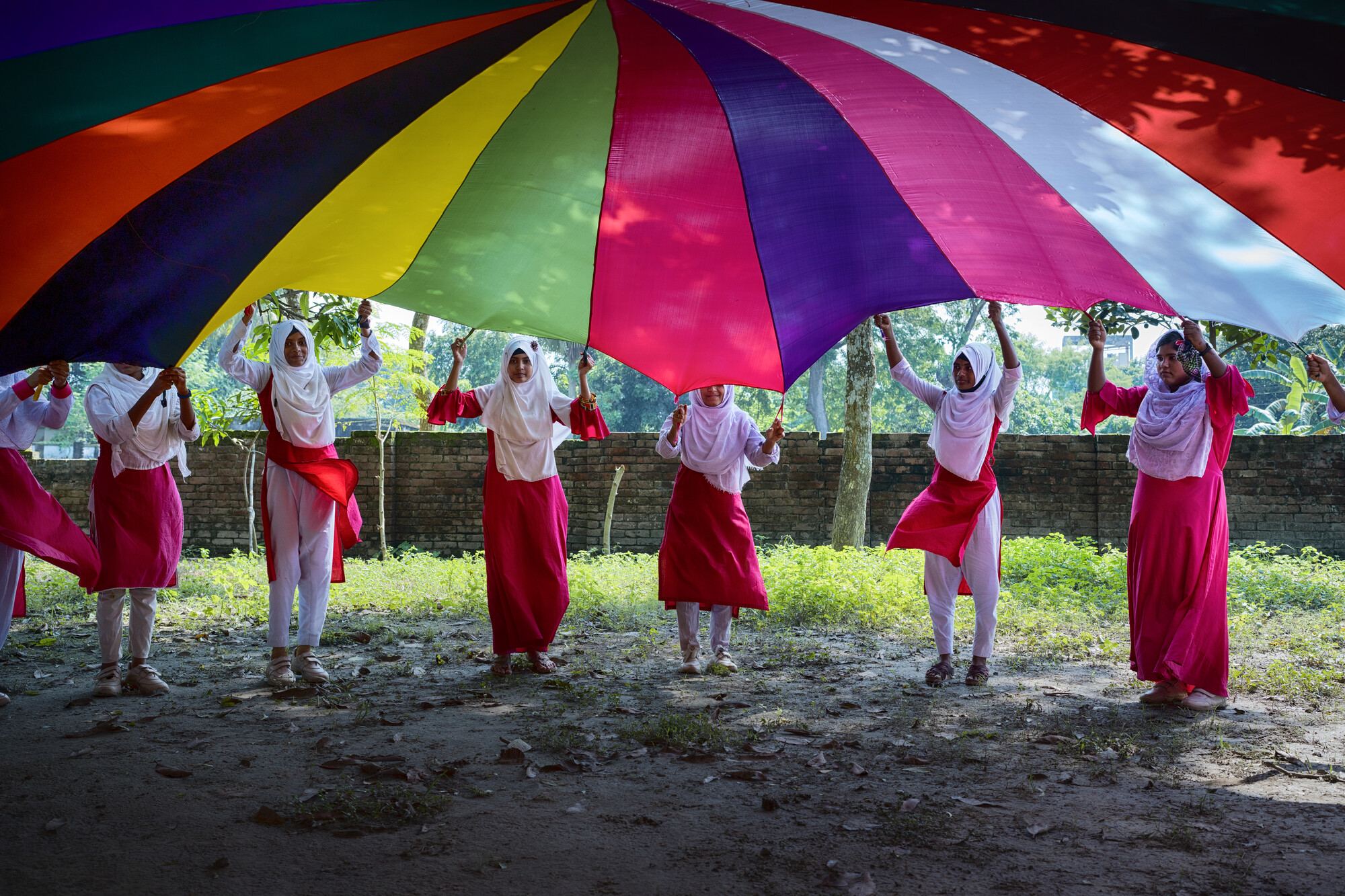 A group of students stand holding a colorful parachute that's open above them.