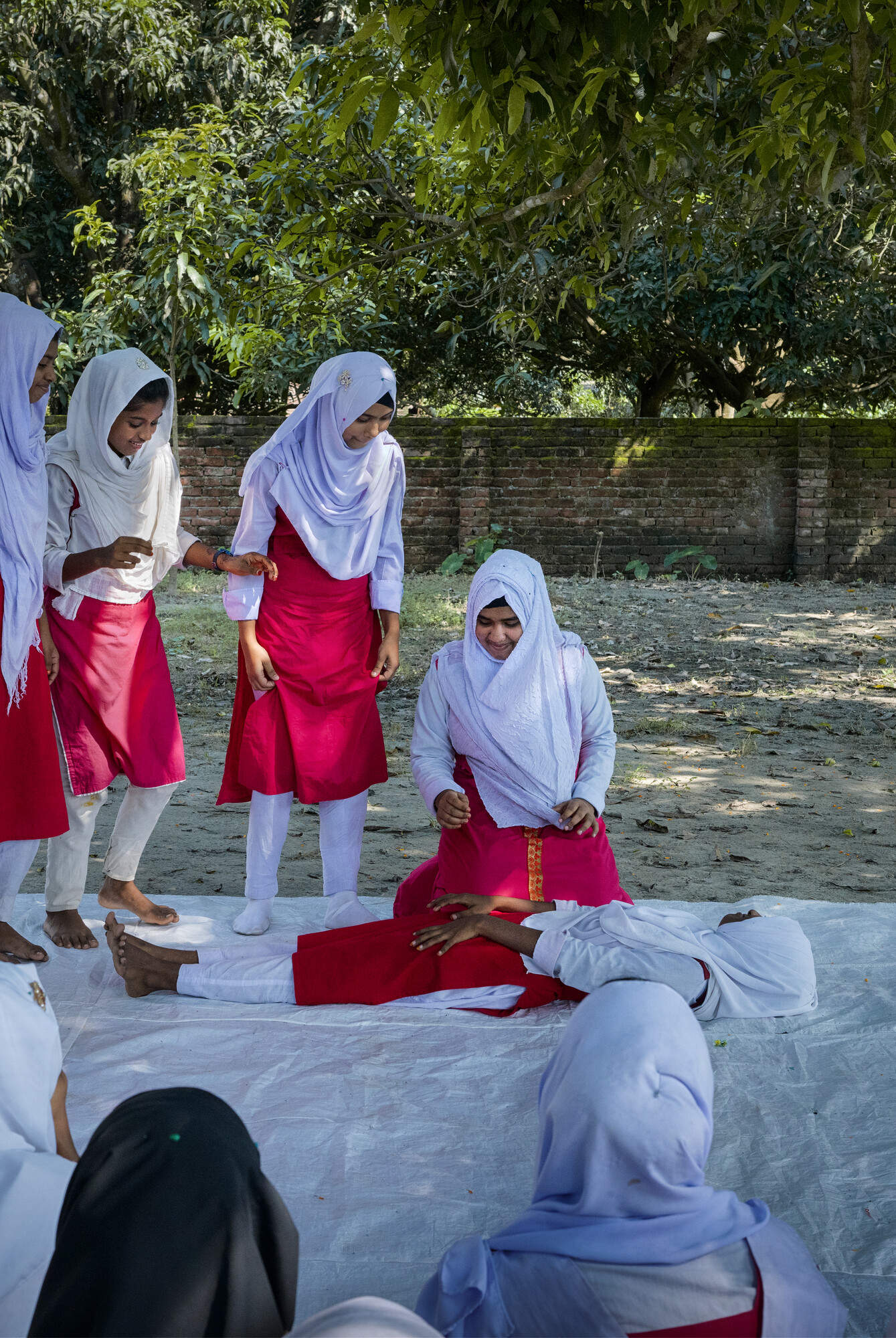 A student lays on their back while another student kneels over them. Other students observe.