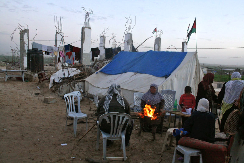 women chatting around fire beside tent and bombed building